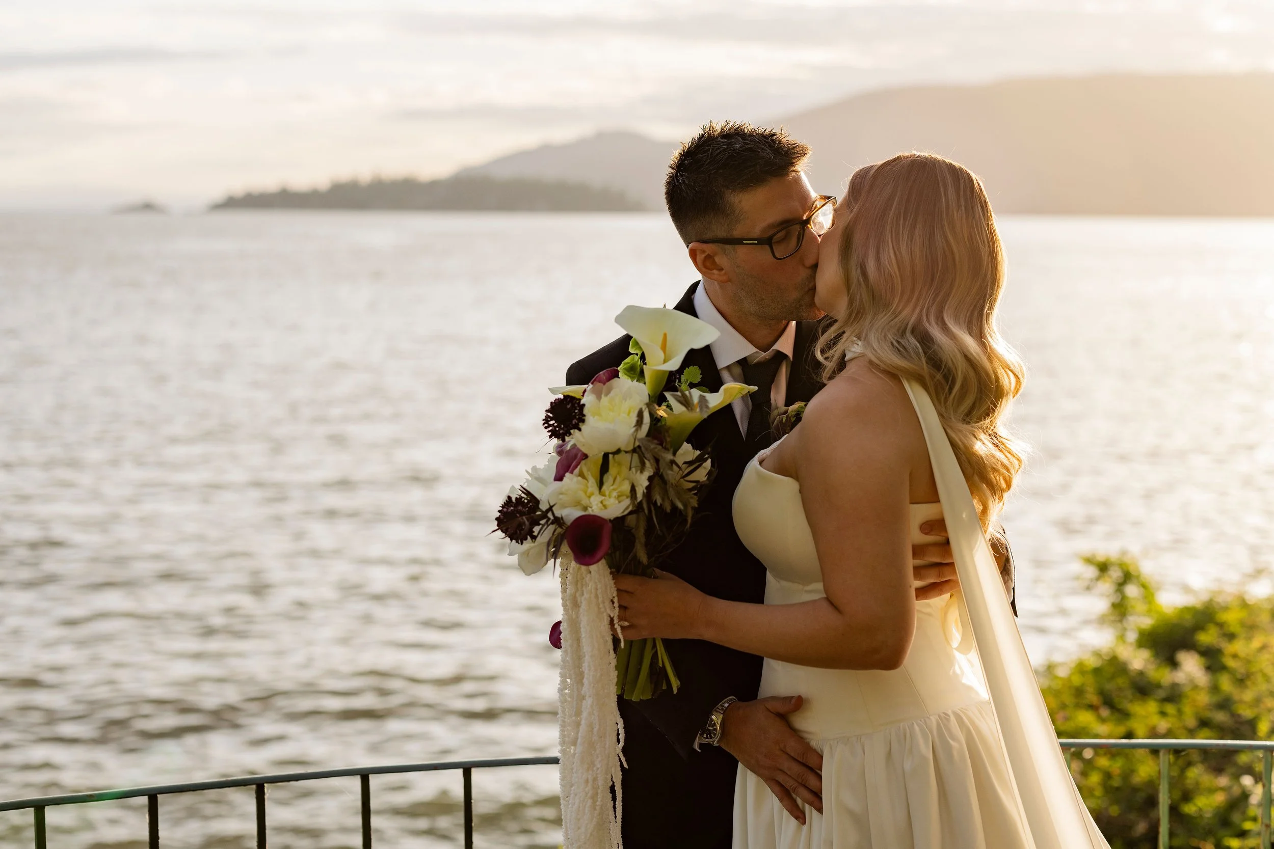 The bride and groom kiss on the shoreline of West Vancouver