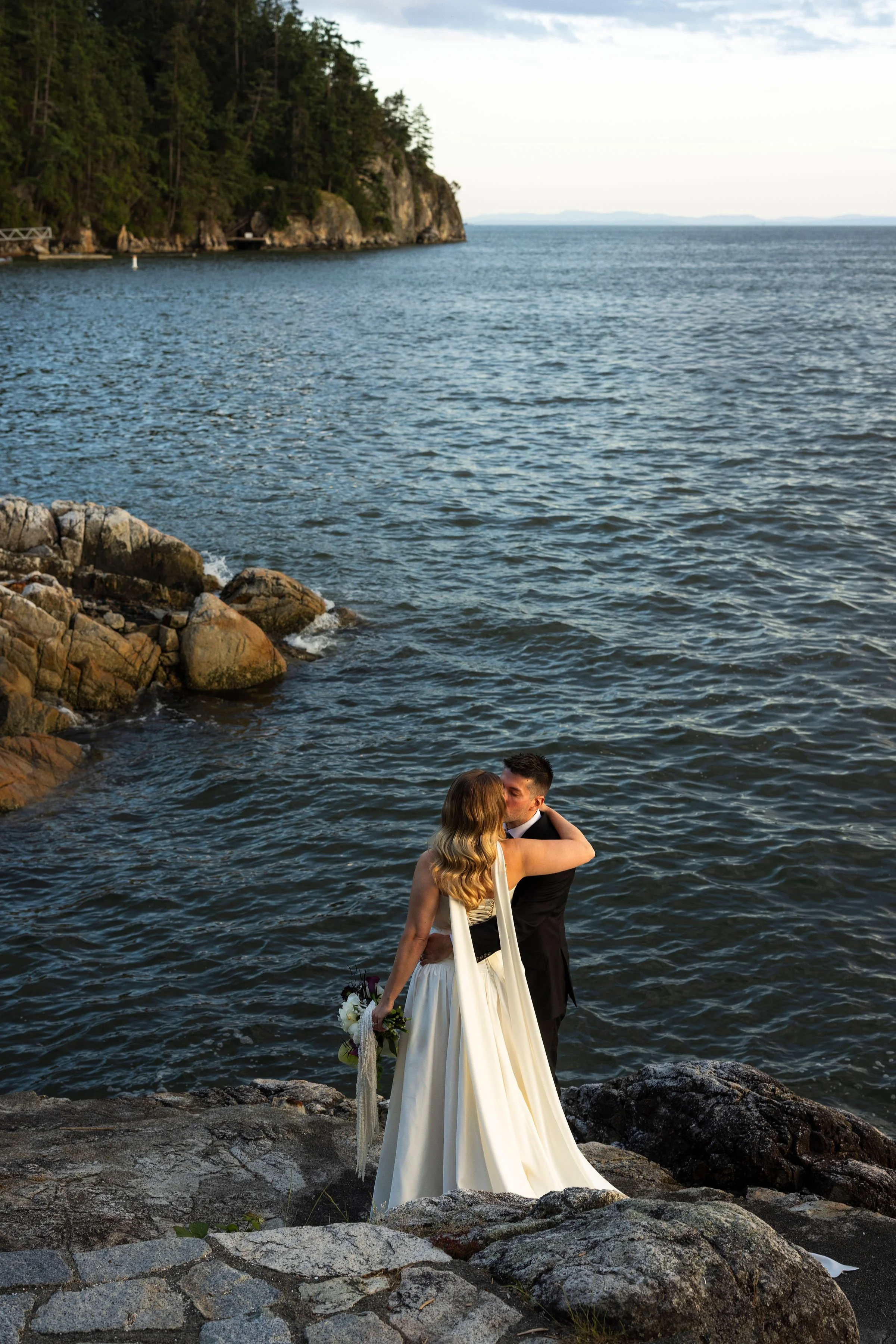 Eloping bride and groom kiss on the rocky Vancouver shore