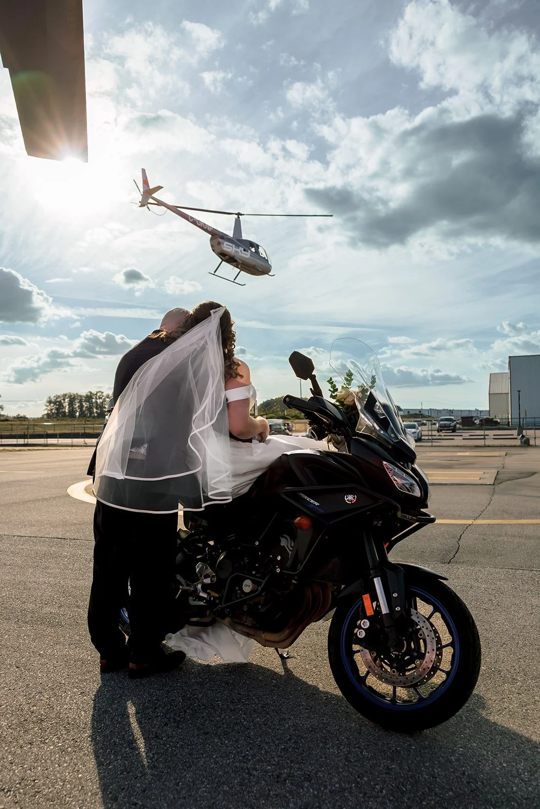 Bride and groom watch a helicopter take off from a motorcycle