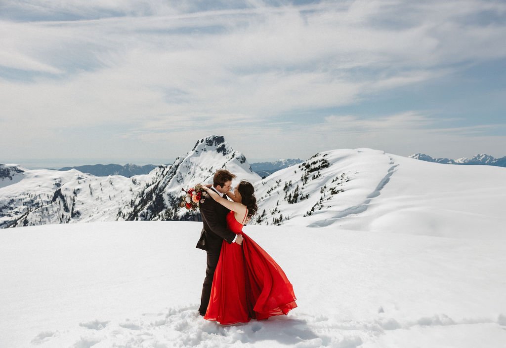 A bride and groom embrace on a snowy mountaintop
