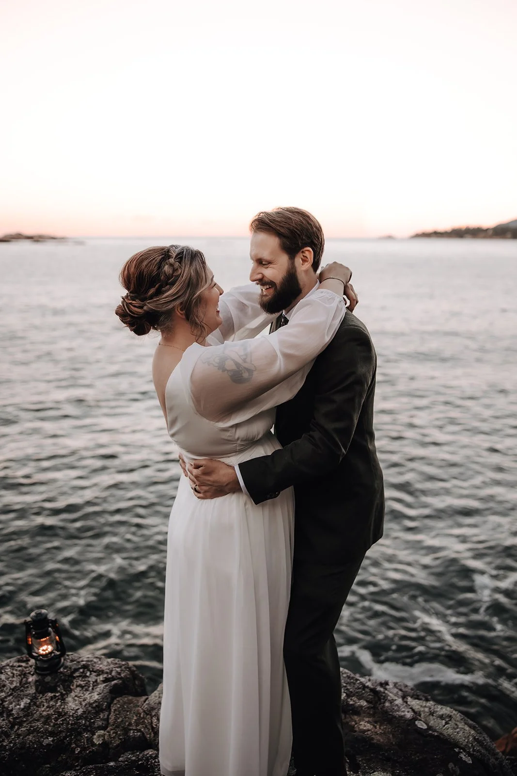 A bride and groom embrace during sunset