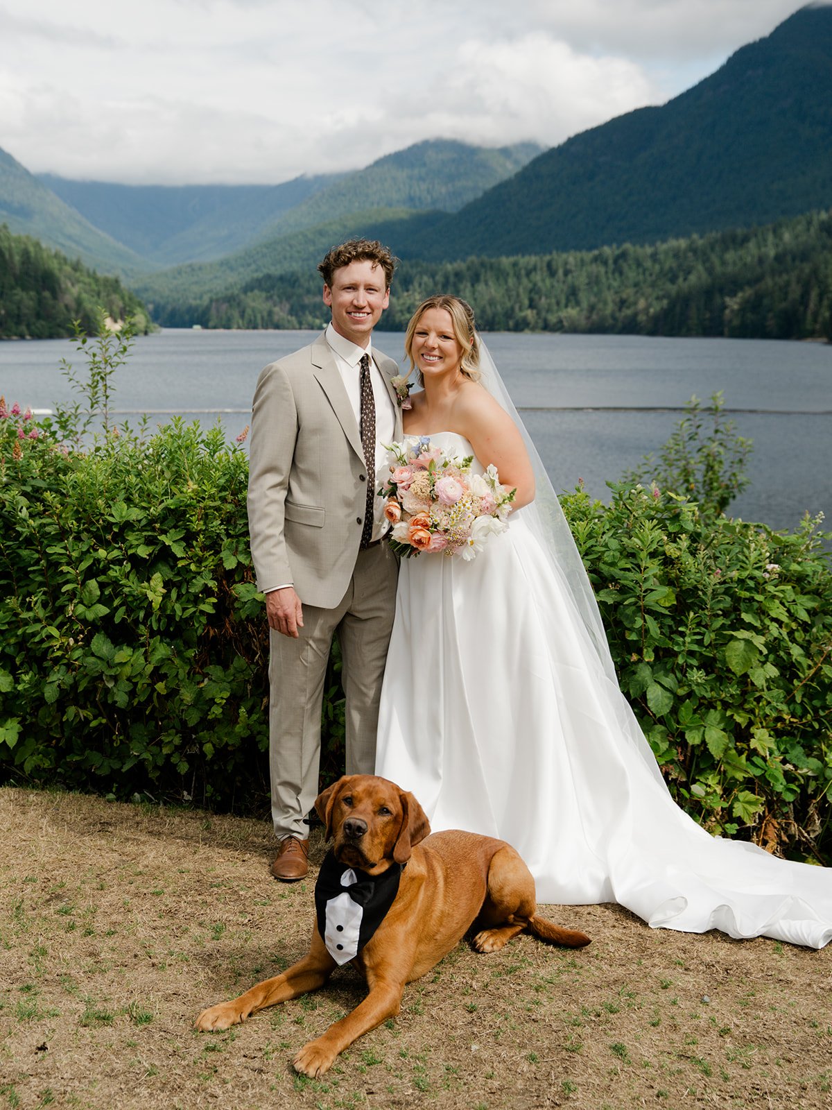 A bride, groom and dog eloping in front of Capilano Lake