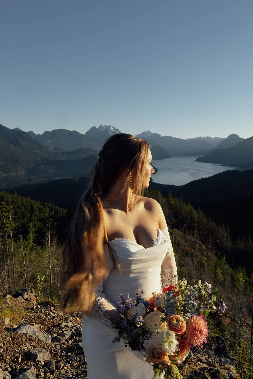 A beautiful bride standing on a mountain with Pitt Lake in the background