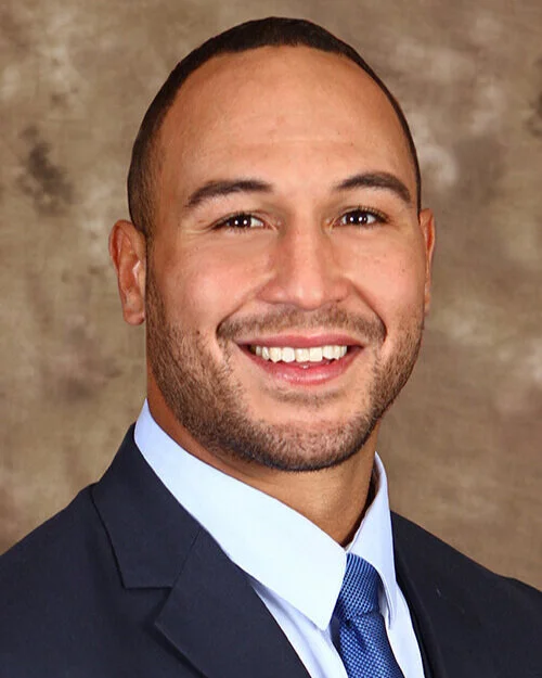 Smiling man in a suit and tie with a neutral background.