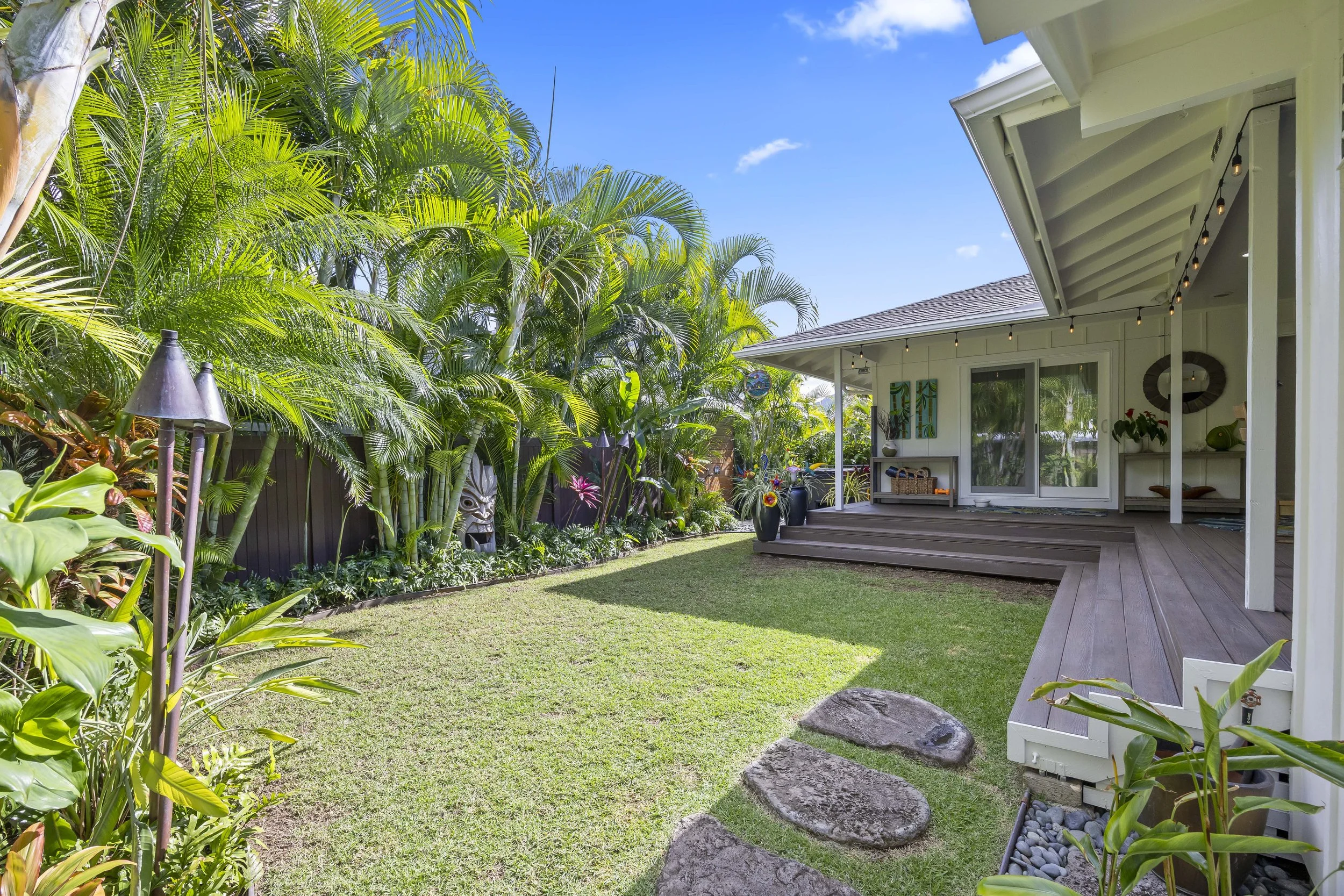 Fully gated back yard with professional landscaping, brass lighting, and copper tiki torches.
