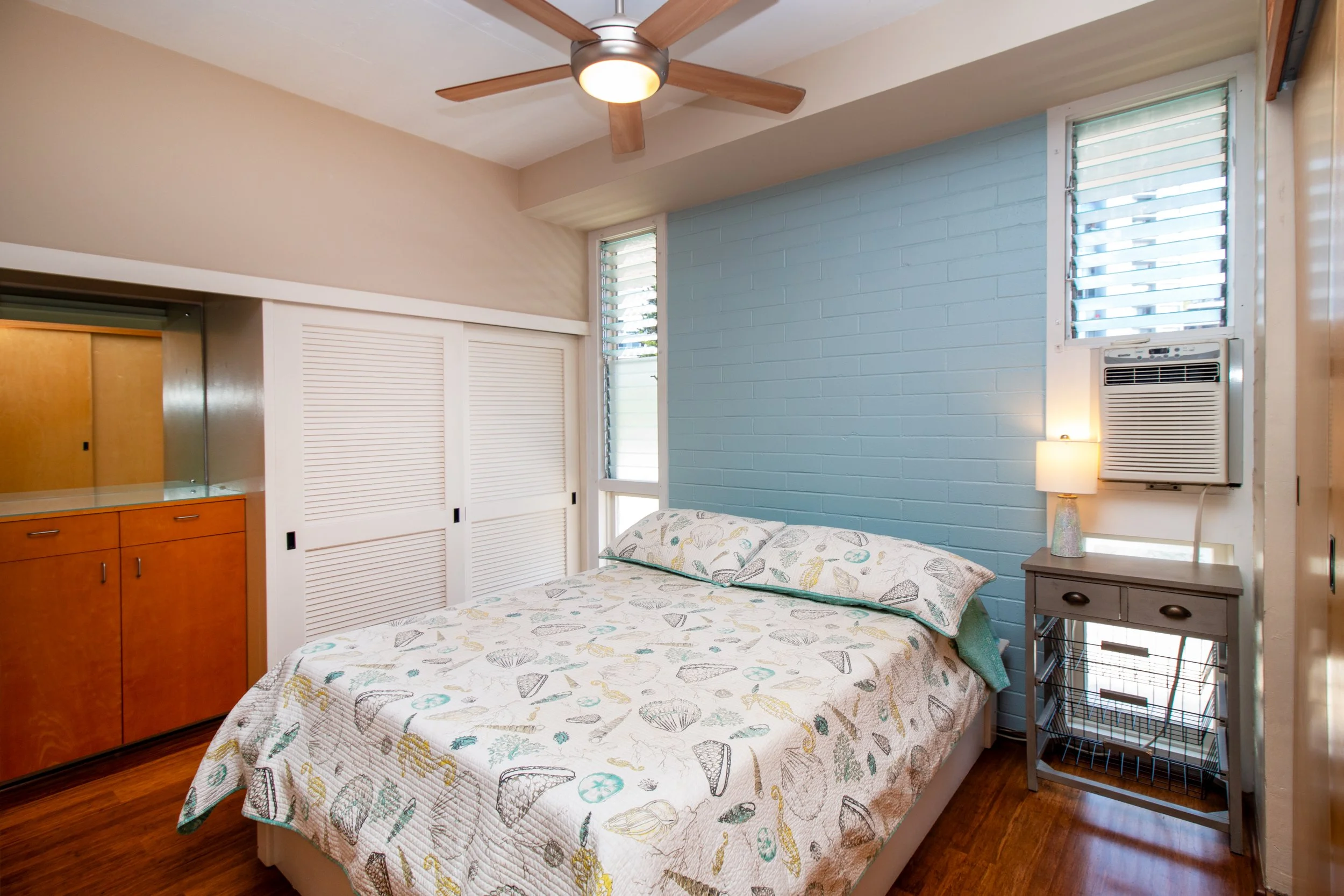 Bedroom with window AC, ceiling fan, and louver windows.