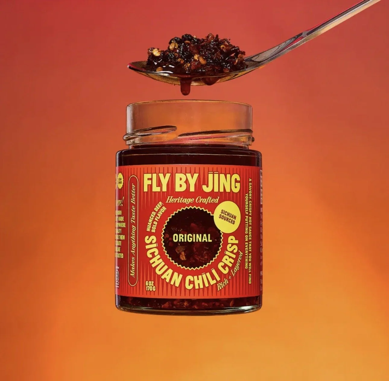 A jar of Fly By Jing Sichuan Chili Crisp with a spoonful above the jar against an orange background.