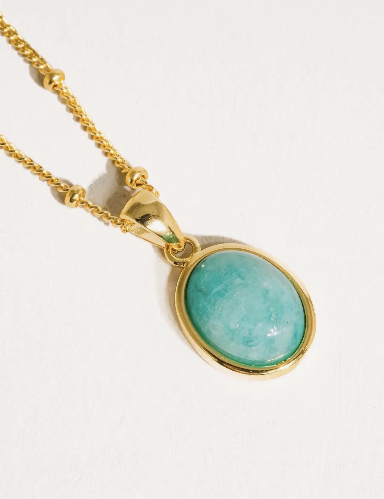 Gold chain necklace with a large oval turquoise pendant.
