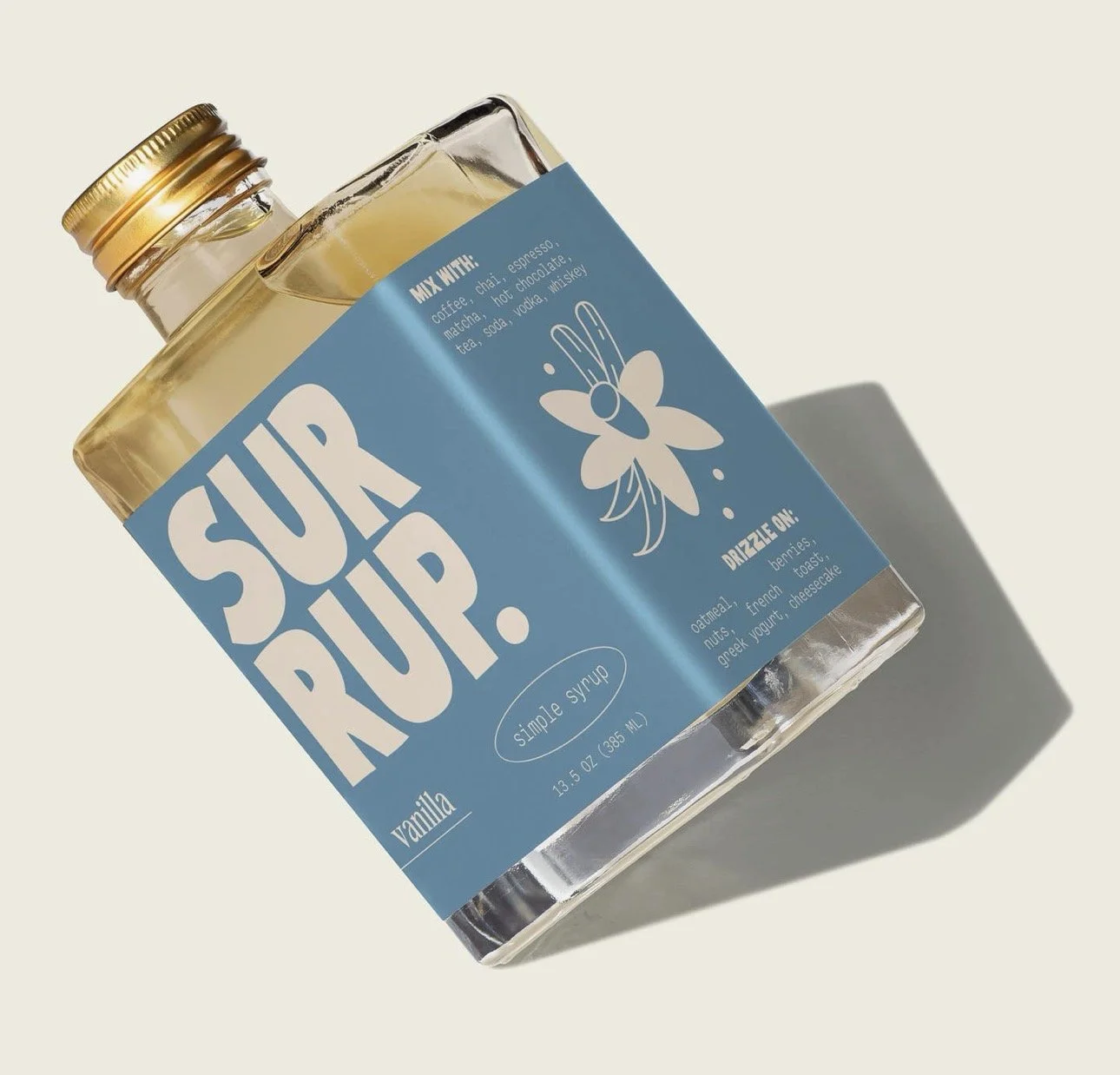 A bottle of vanilla simple syrup with a blue label and a white bee illustration, labeled "SUGAR DROP," placed on a light-colored background casting a shadow.