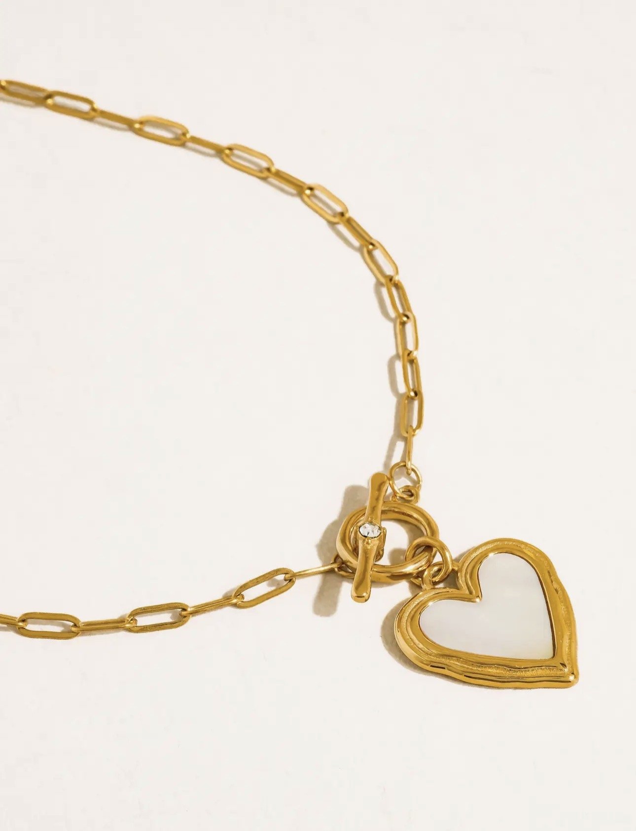 Gold necklace with a heart-shaped pendant and a small gemstone, laid on a white surface.