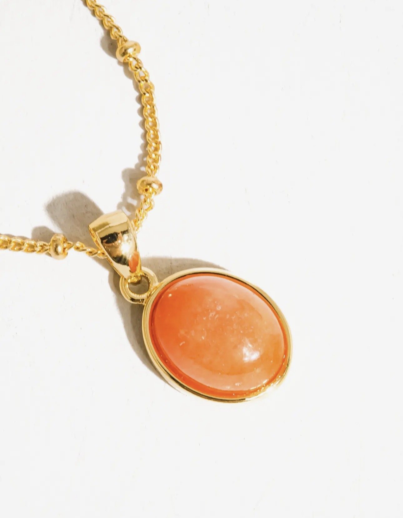 Gold necklace with a round orange pendant on a white background.
