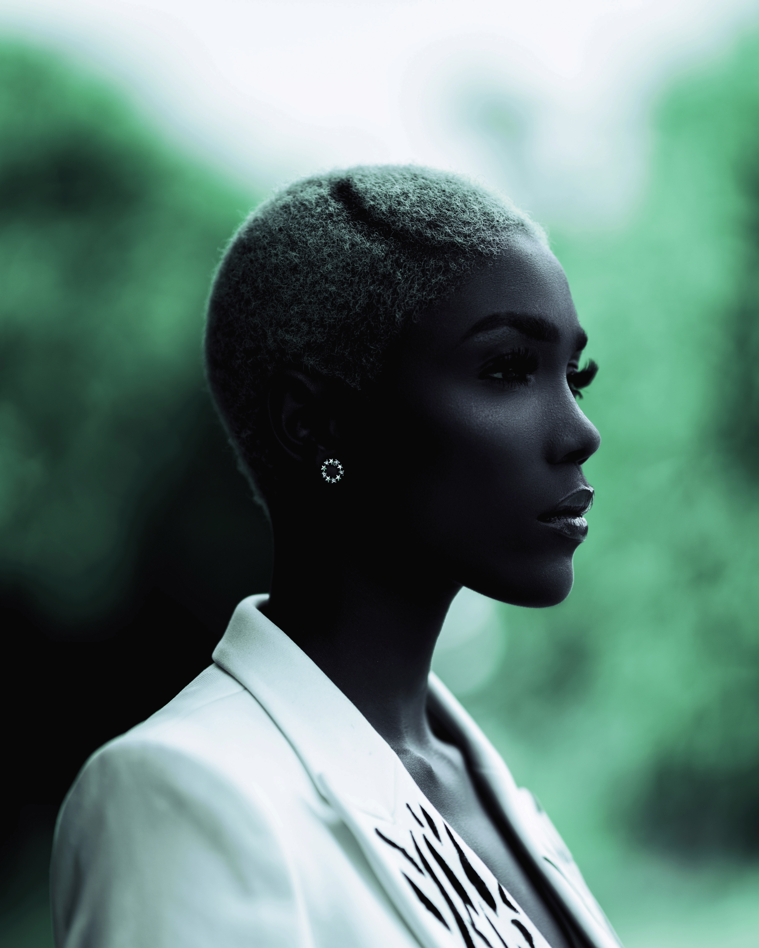 Side profile of a woman with dark skin and highlighted hair in an outdoor setting.