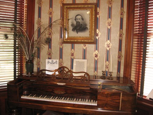 A Chickering piano with peacock feathers and a portrait hanging on the wall.