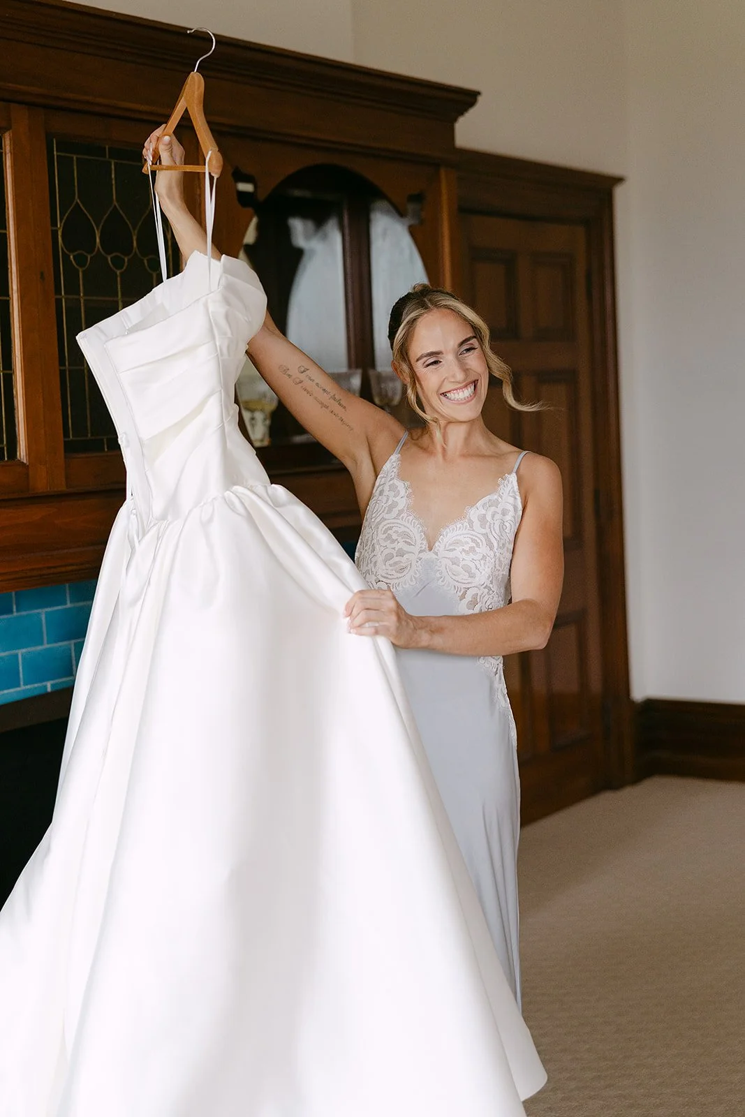 A woman in a wedding dress holding up her wedding gown and smiling indoors.