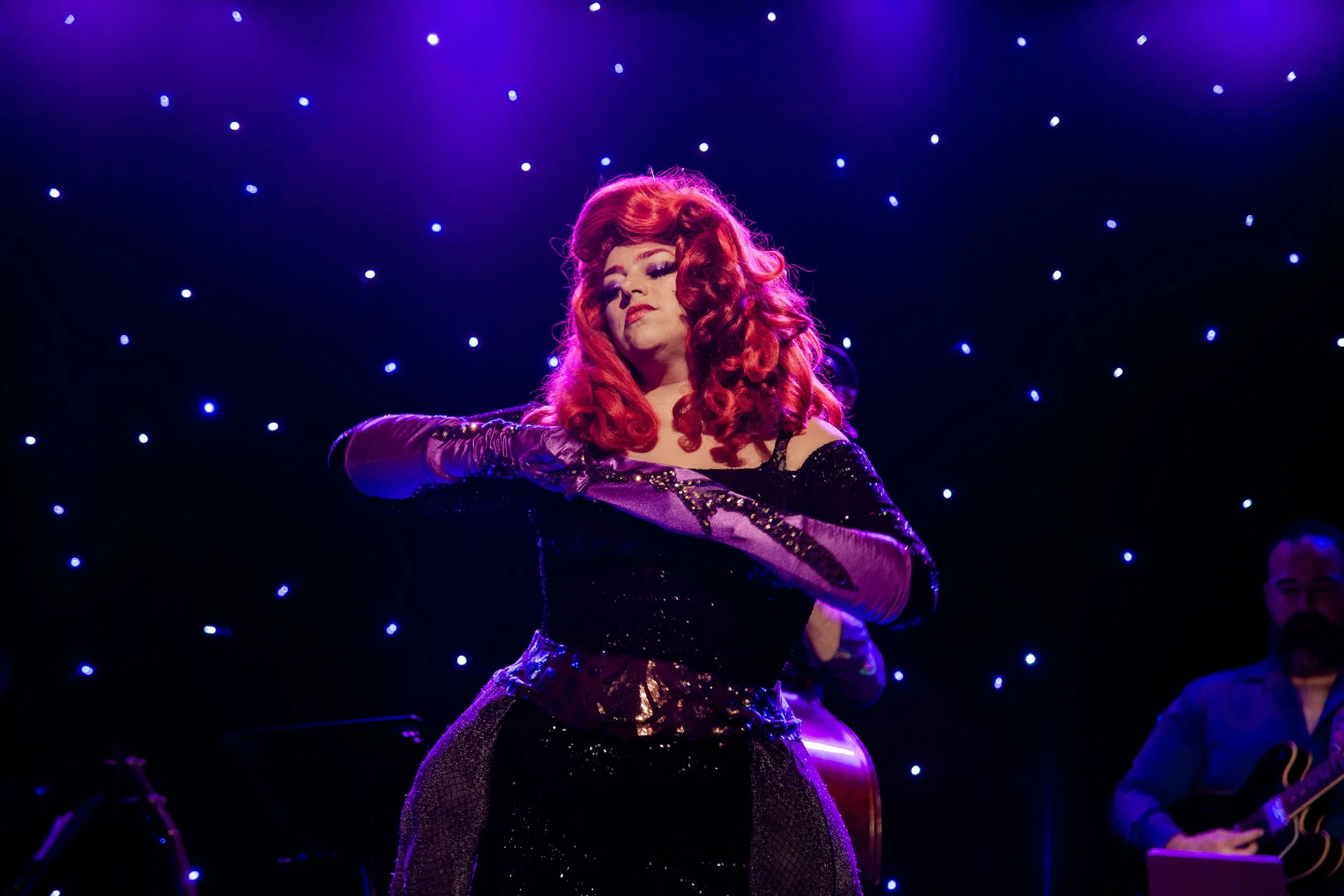 Mae Lust strips a purple, sequined glove in black gown with purple tentacles dangling from a belt