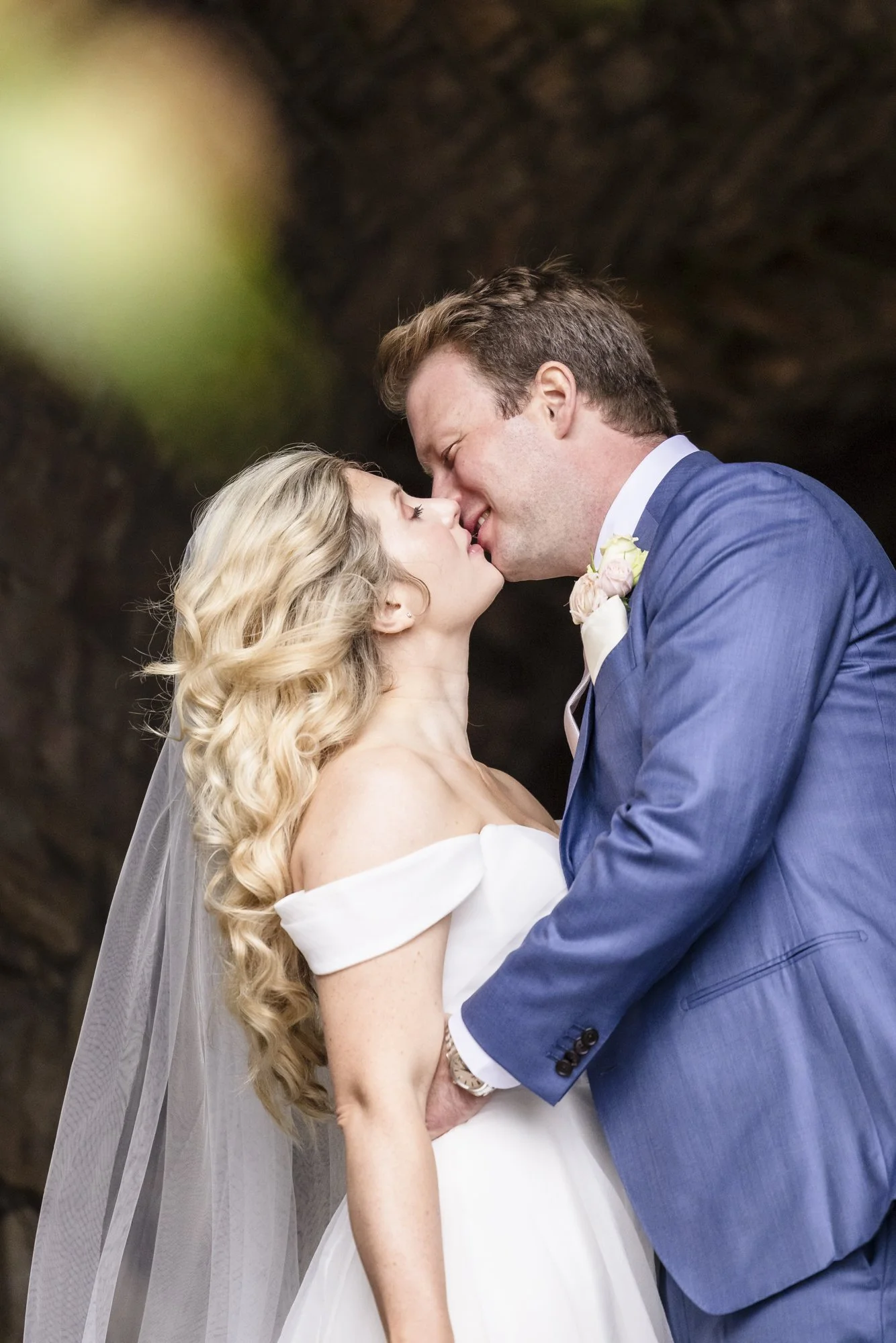 Et bryllup av kjærlighet mellom en brud i hvitt og en brudgom i blått dress, som kysser hverandre.