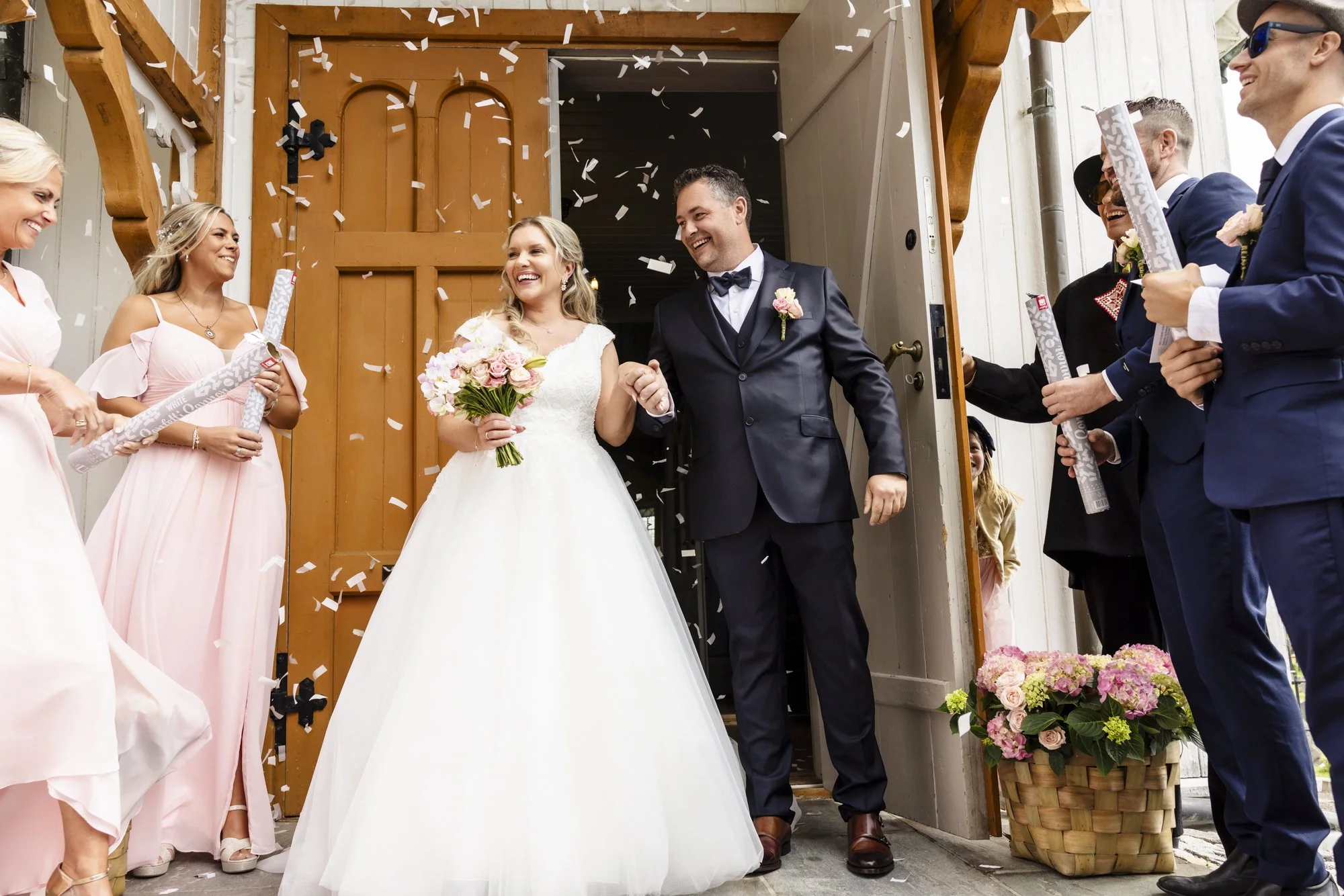 Nydelige brudepar som smiler og holder hender, omringet av venner og familie som kaster konfetti under utgang for bryllupet.