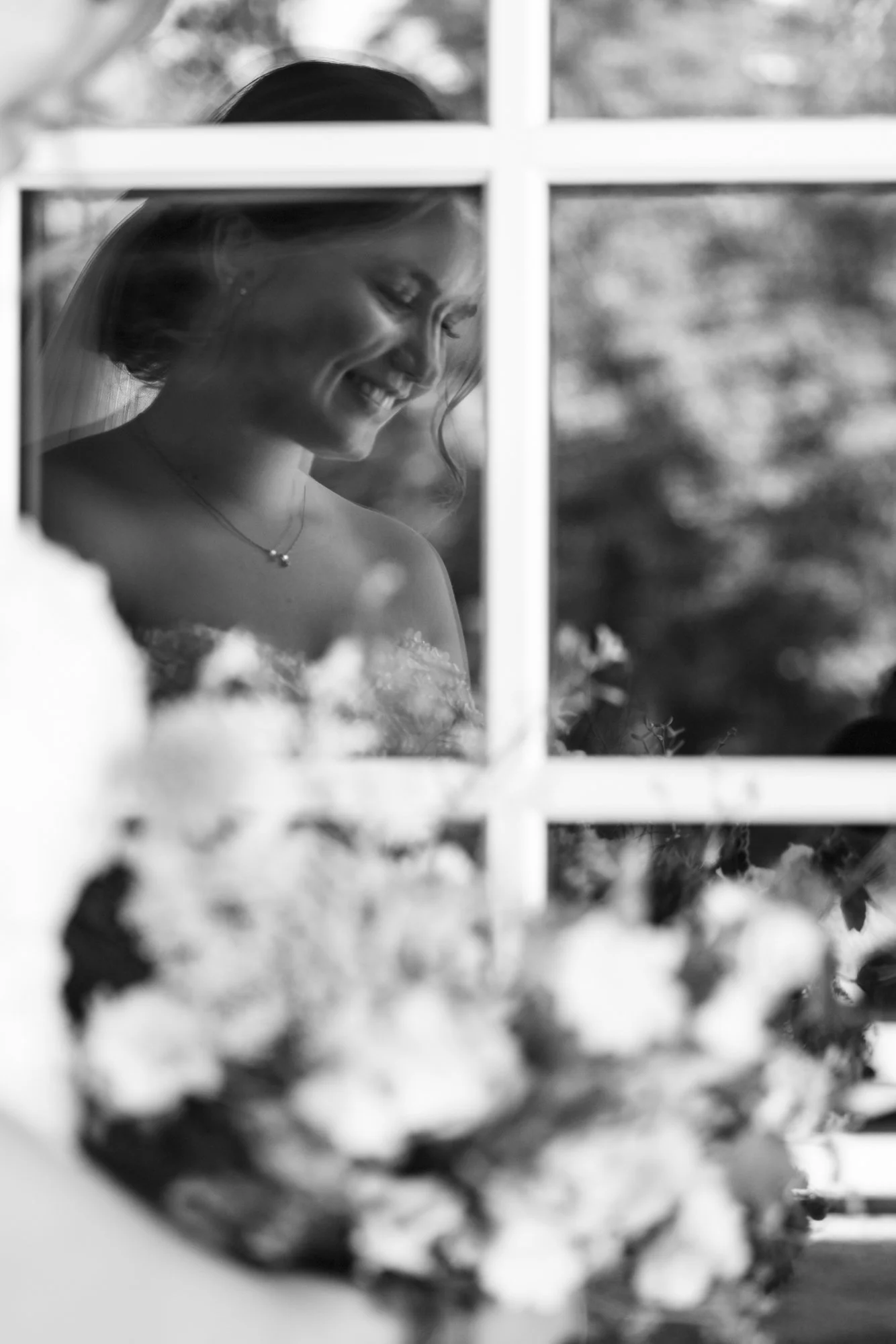 En gravid kvinne smiler mens hun ser ut av et vindu, i svart-hvitt.