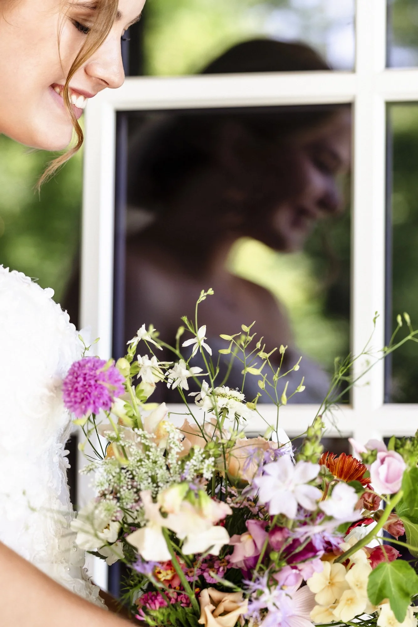 En kvinne som smiler og holder en stor bukett med blomster. Det er et vindu eller speil bak henne.