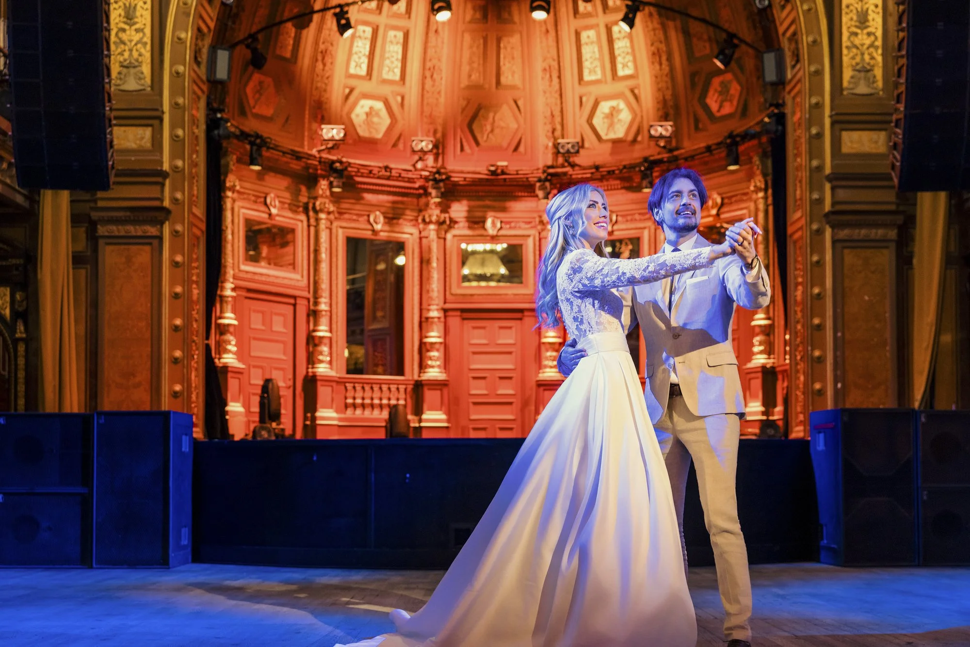 Et par danser offentlig i en historisk dansesal med utsmykket treverk og høyt tak.