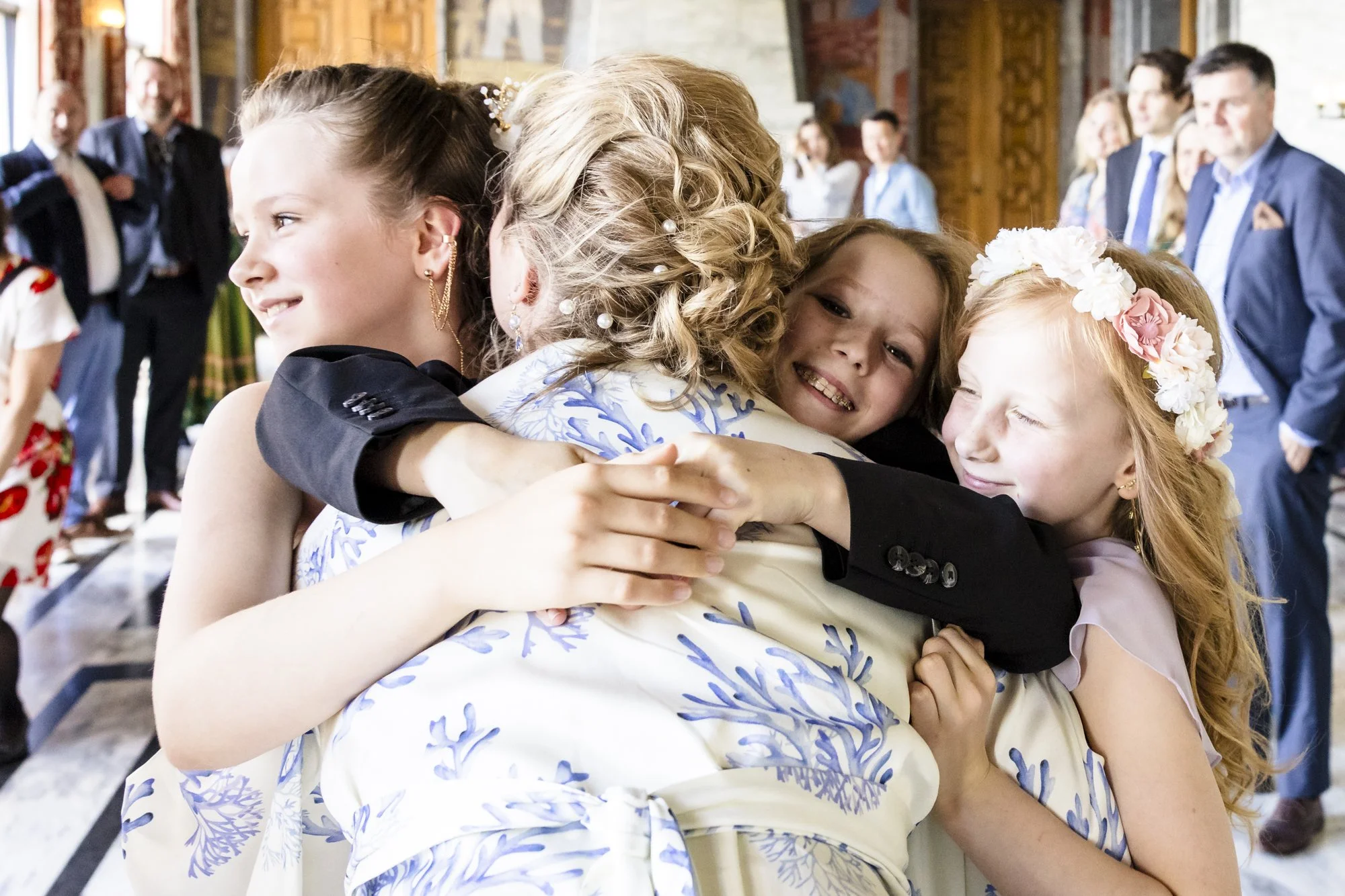 Ei gruppe av glade unge jenter og kvinner omfavner hverandre i en gruppe, midt i et rom med trevegger og folk som ser på, i en festlig setting.