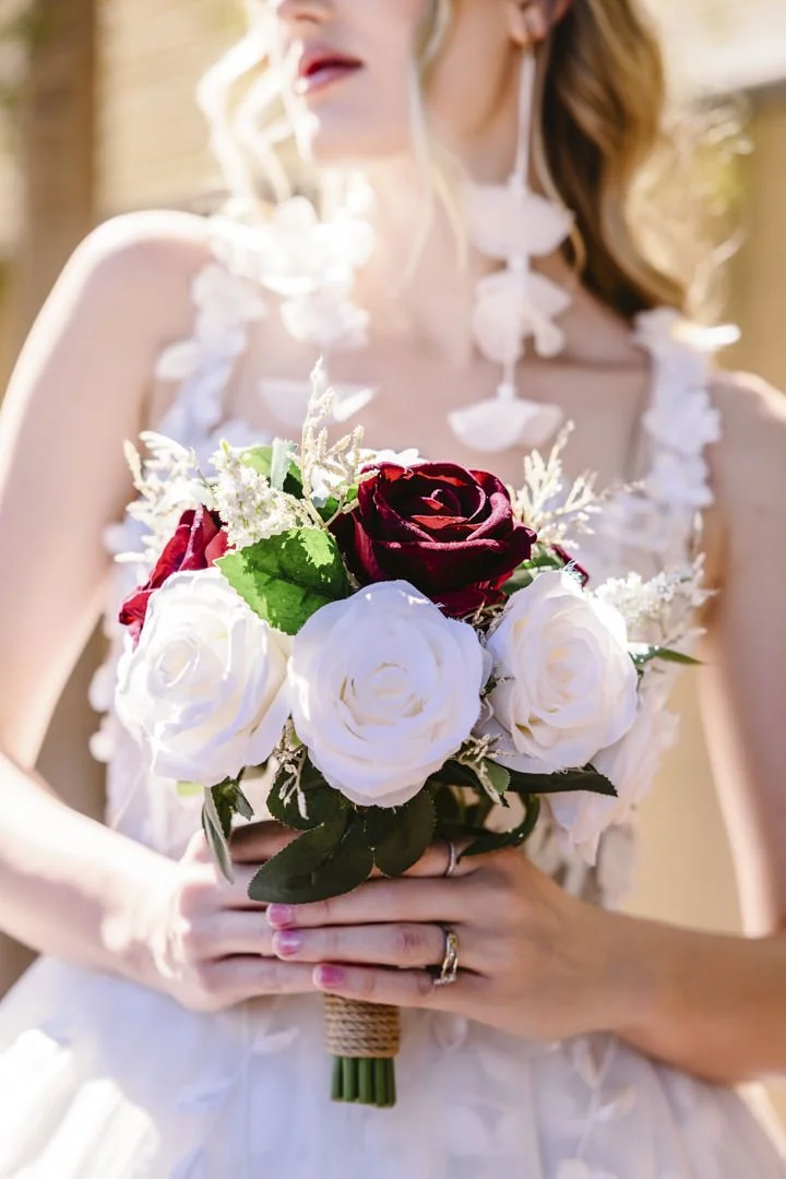 Kvinner i brudekjole holder en bryllupskrans med hvite og røde roser.