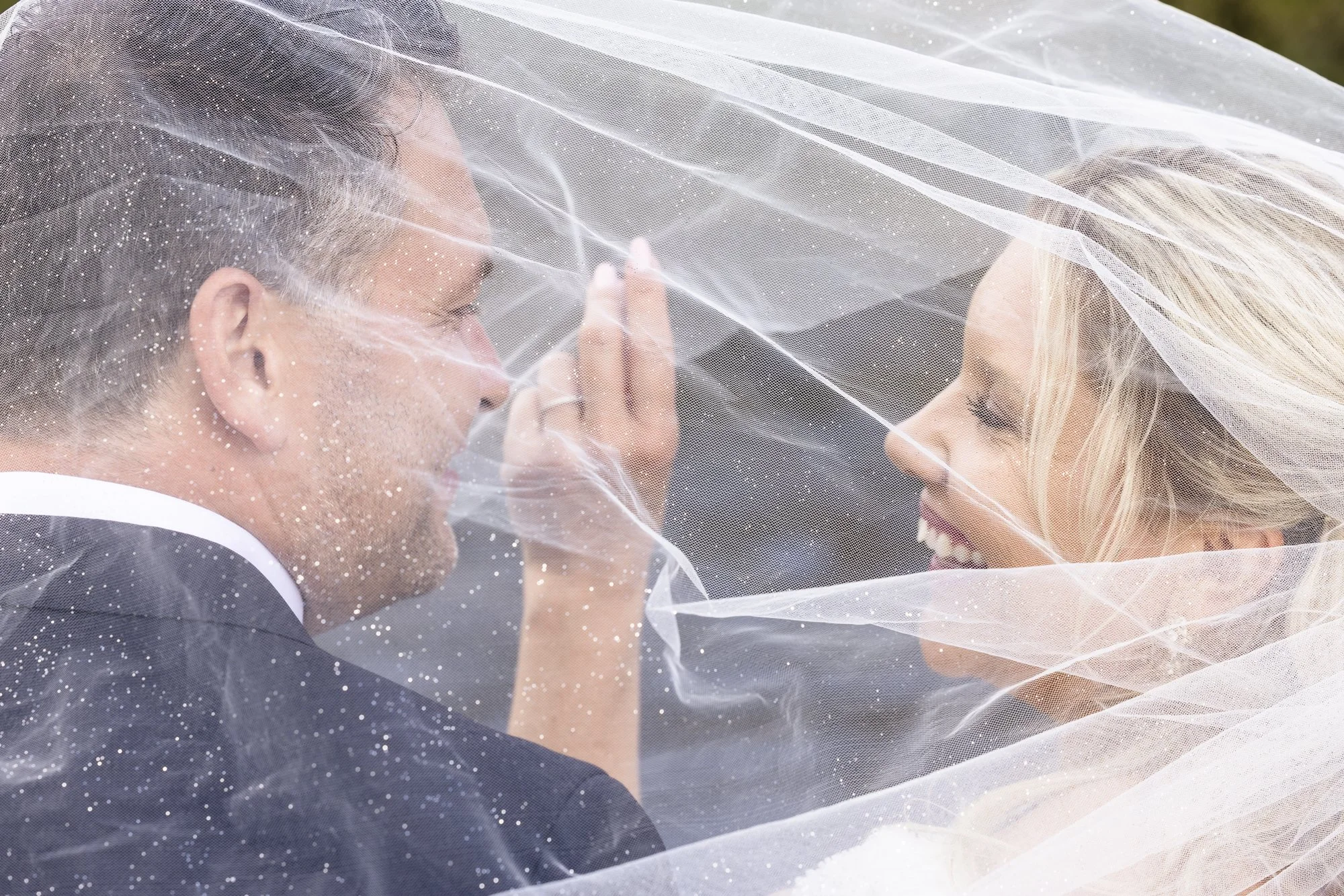 Et par under bryllup, dekket av en tynn, hvit brudekjole. De smiler til hverandre under et øyeblikk, dekket av en gjennomsiktig hvit brudebluse.