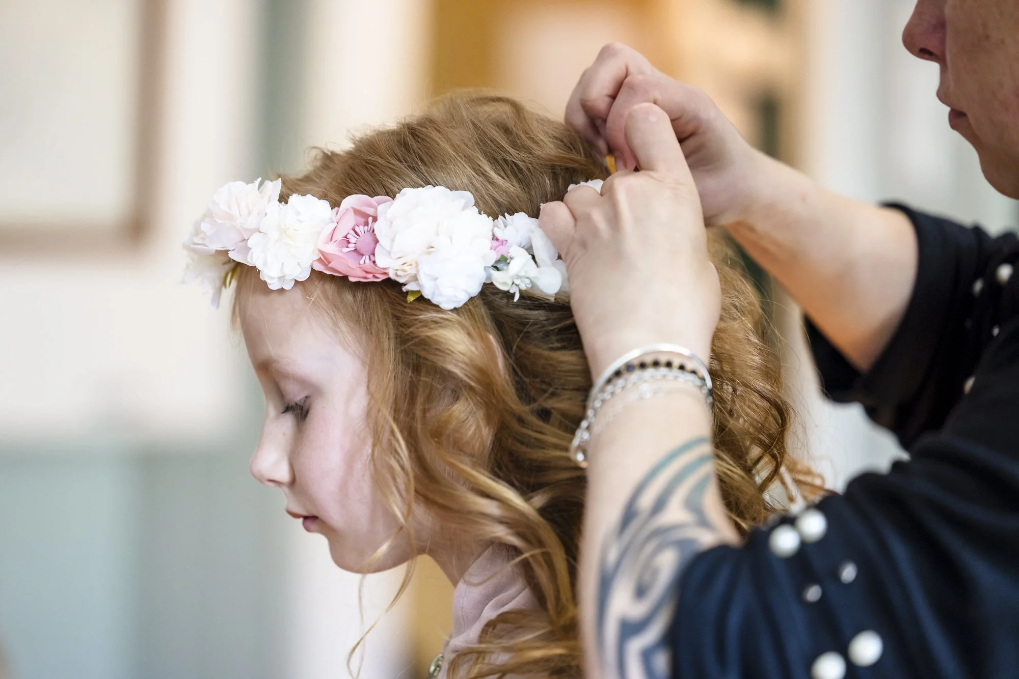 En jente med rødt hår får en blomsterkrans plassert på hodet av en voksen kvinne.