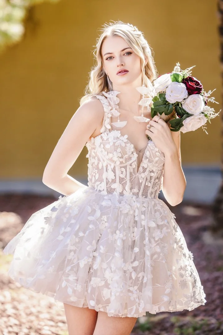 En kvinne i en hvit blomstrete kjole holder en blomsterbukett av roser.