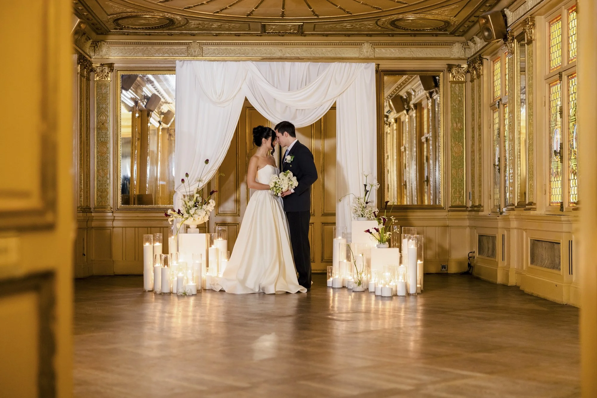 Et brudepar står sammen i en dekorert seremonirom med stearinlys og blomster.