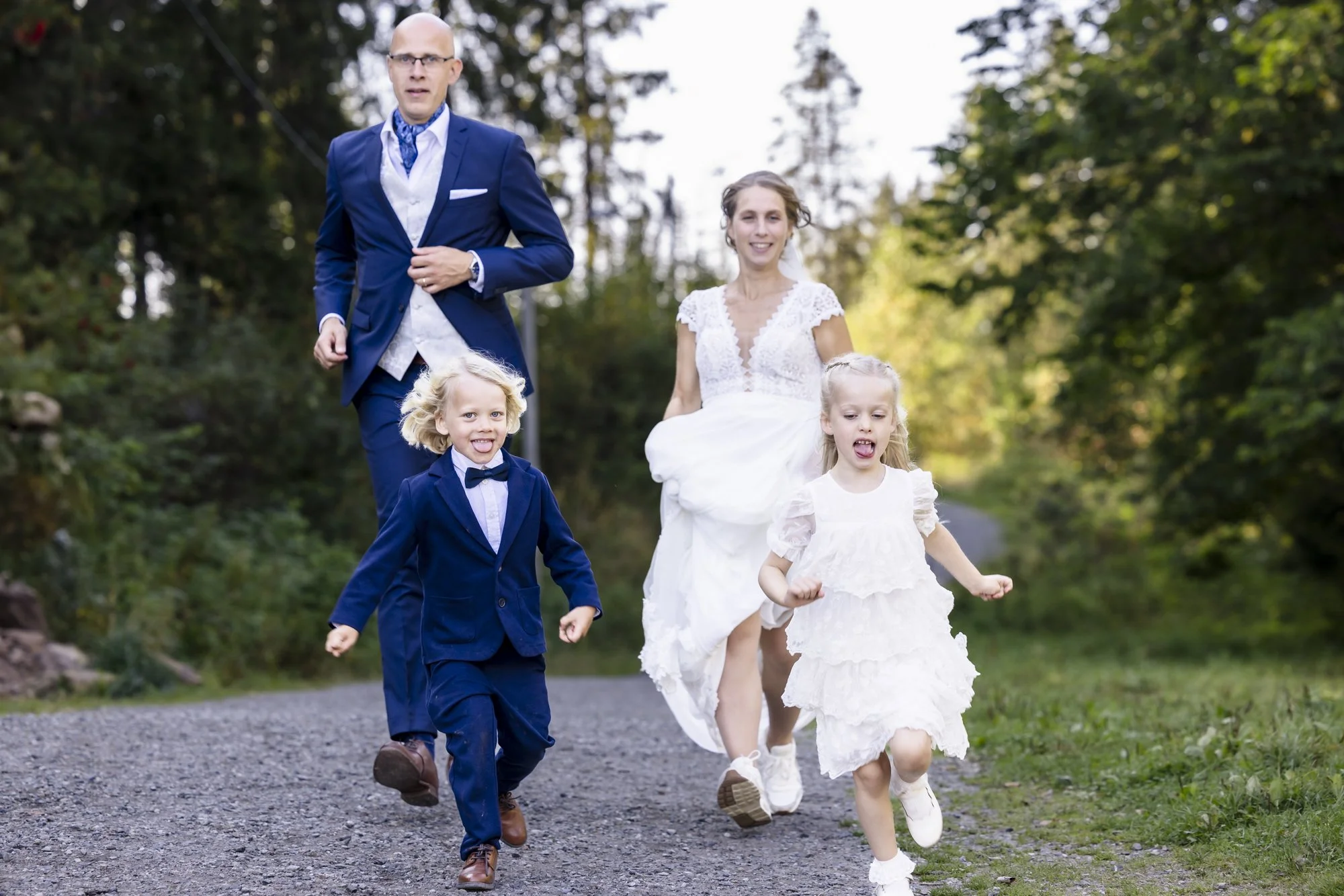 En familie på fire kledd i formelle klær, går på en grusvei omgitt av grønne trær, det ser ut som å ha en spesiell anledning.