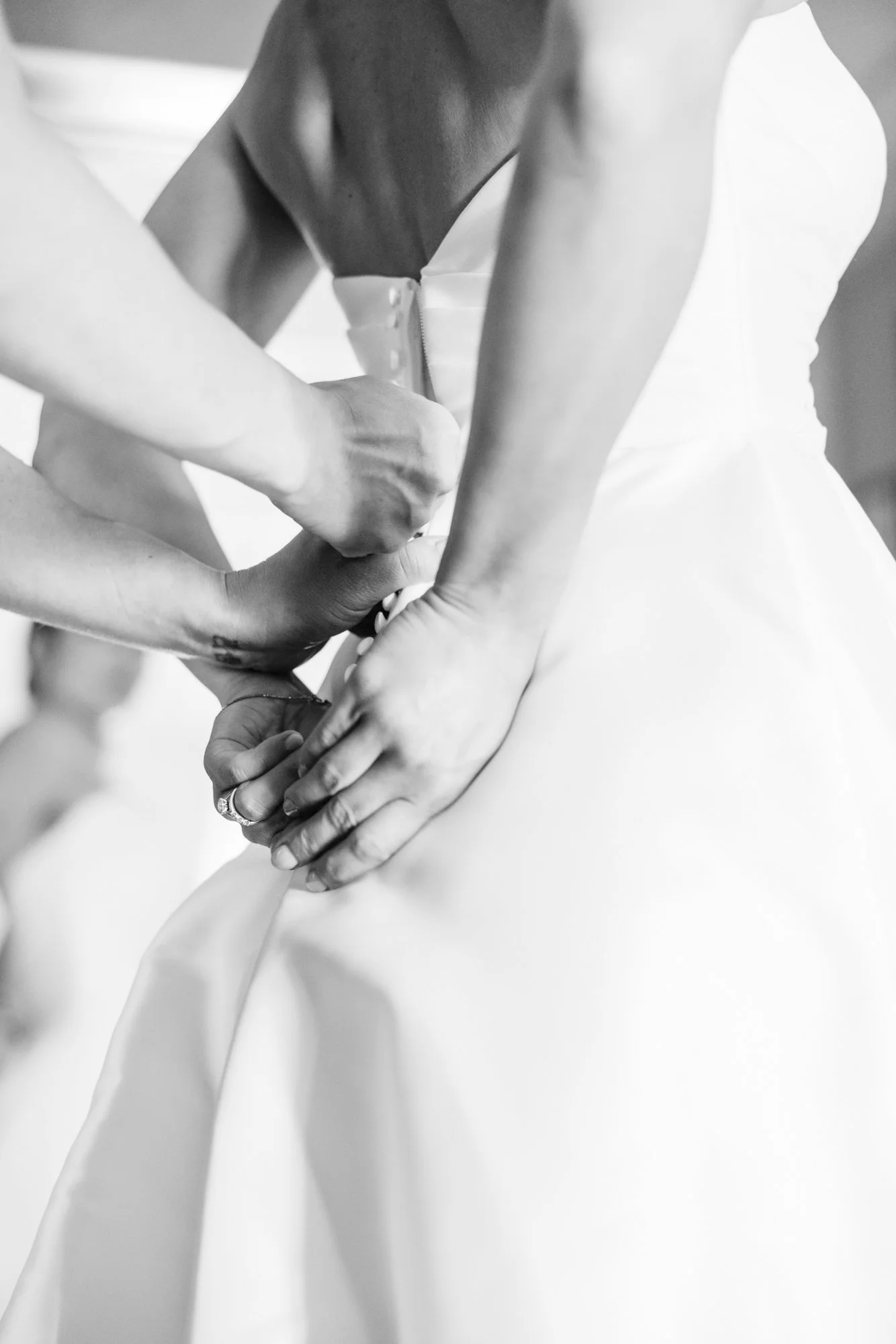 Bilde av en brud som får hjelp med å knappe kjolen foran, i svart-hvitt.