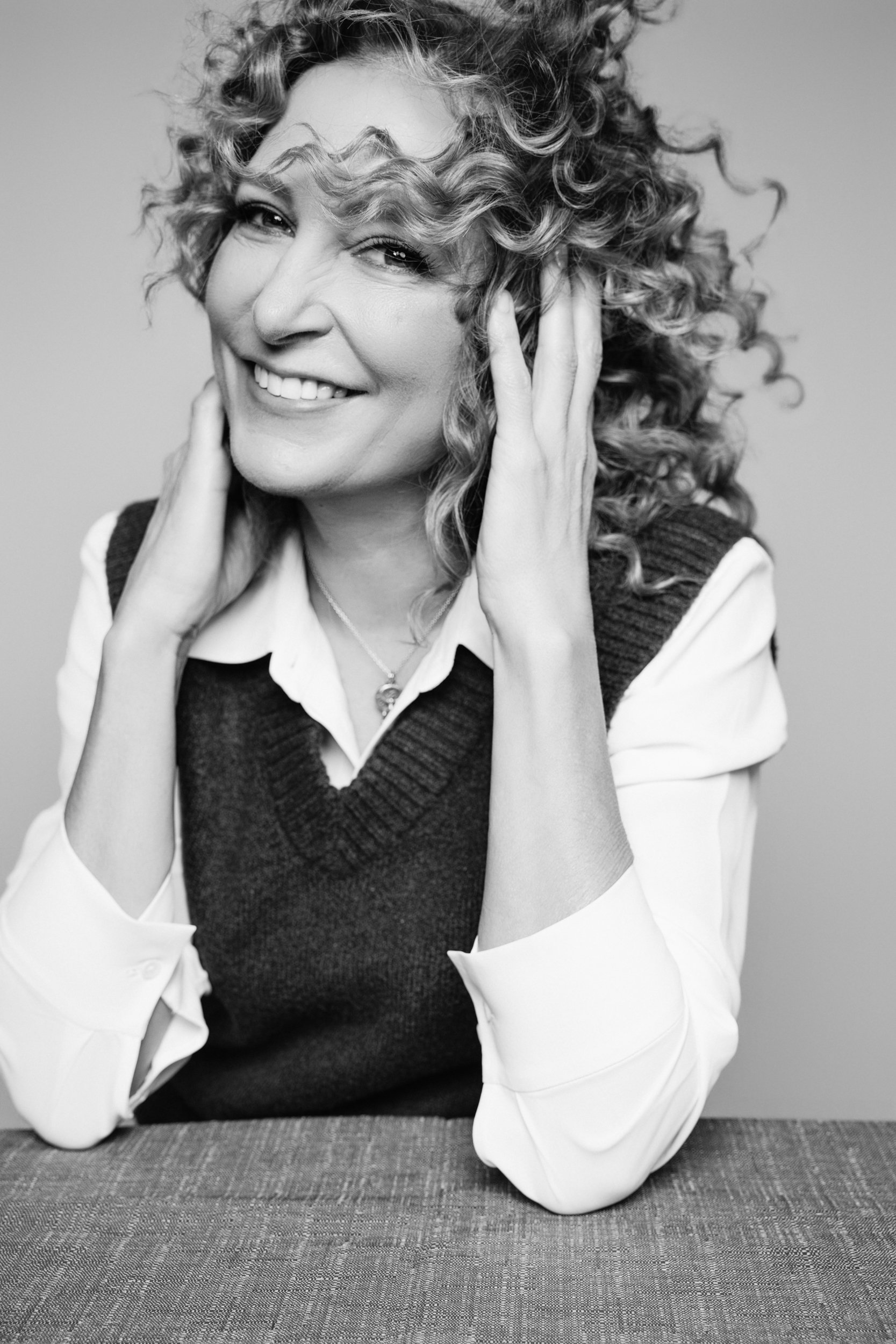 Black and white close-up of an internal medicine doctor laughing with curly hair blowing across her face, emphasizing authentic connection.