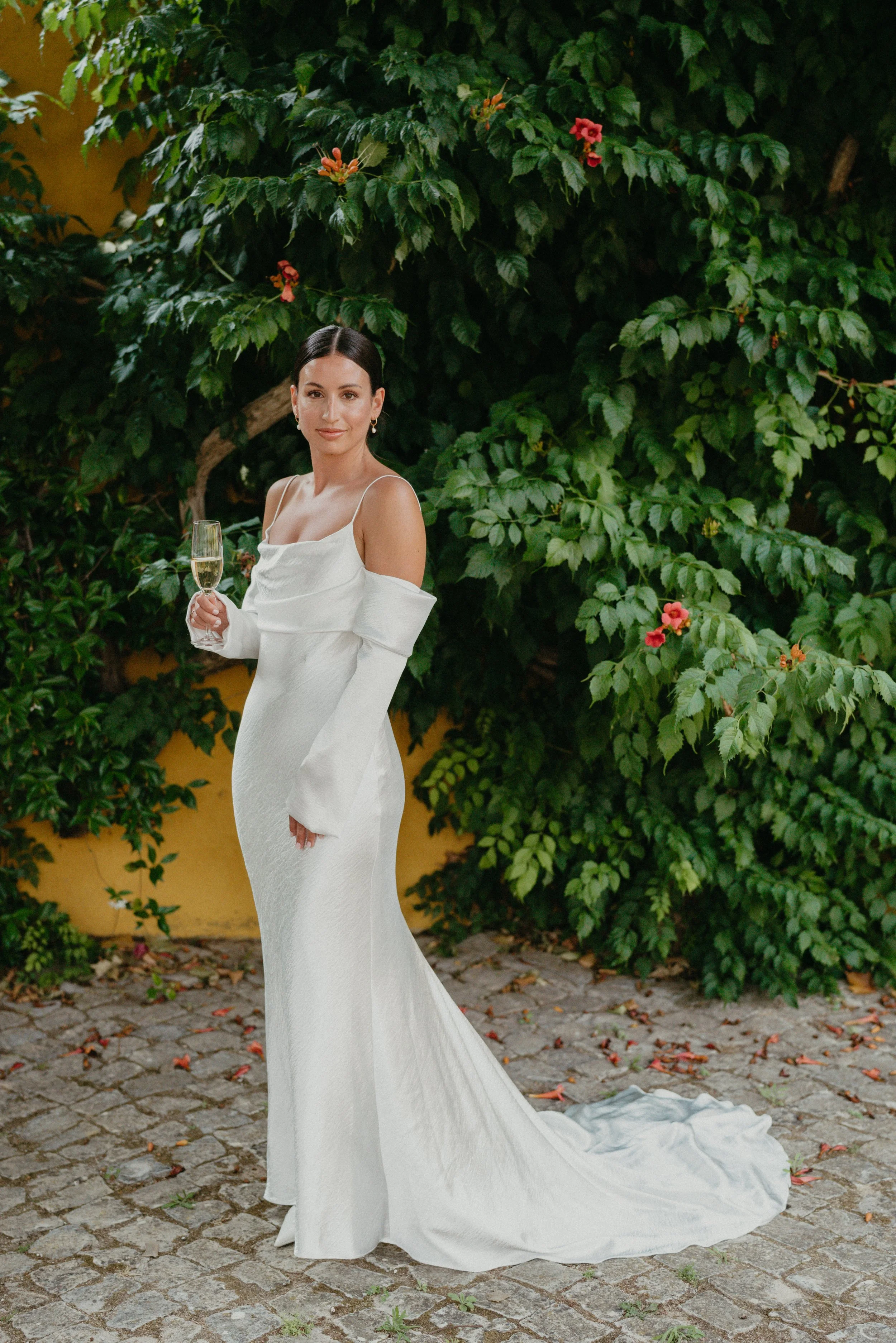 Bride portrait in elegant minimalist wedding dress holding champagne at Quinta de Sant’Ana wedding venue in Mafra Portugal