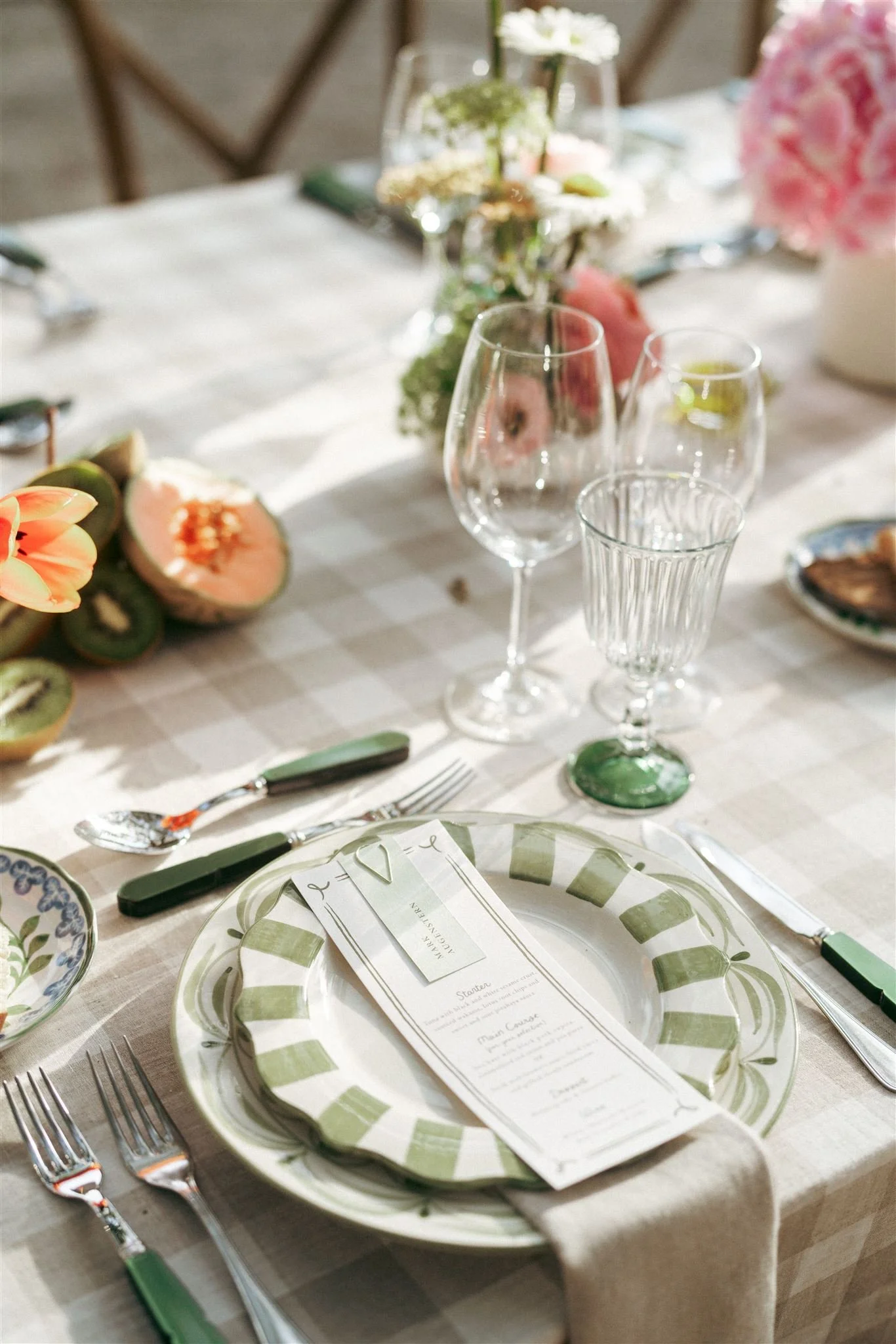 Close-up of a place setting with custom green ceramic plates, wedding menu, and glassware at an outdoor wedding dinner at Herdade do Peru