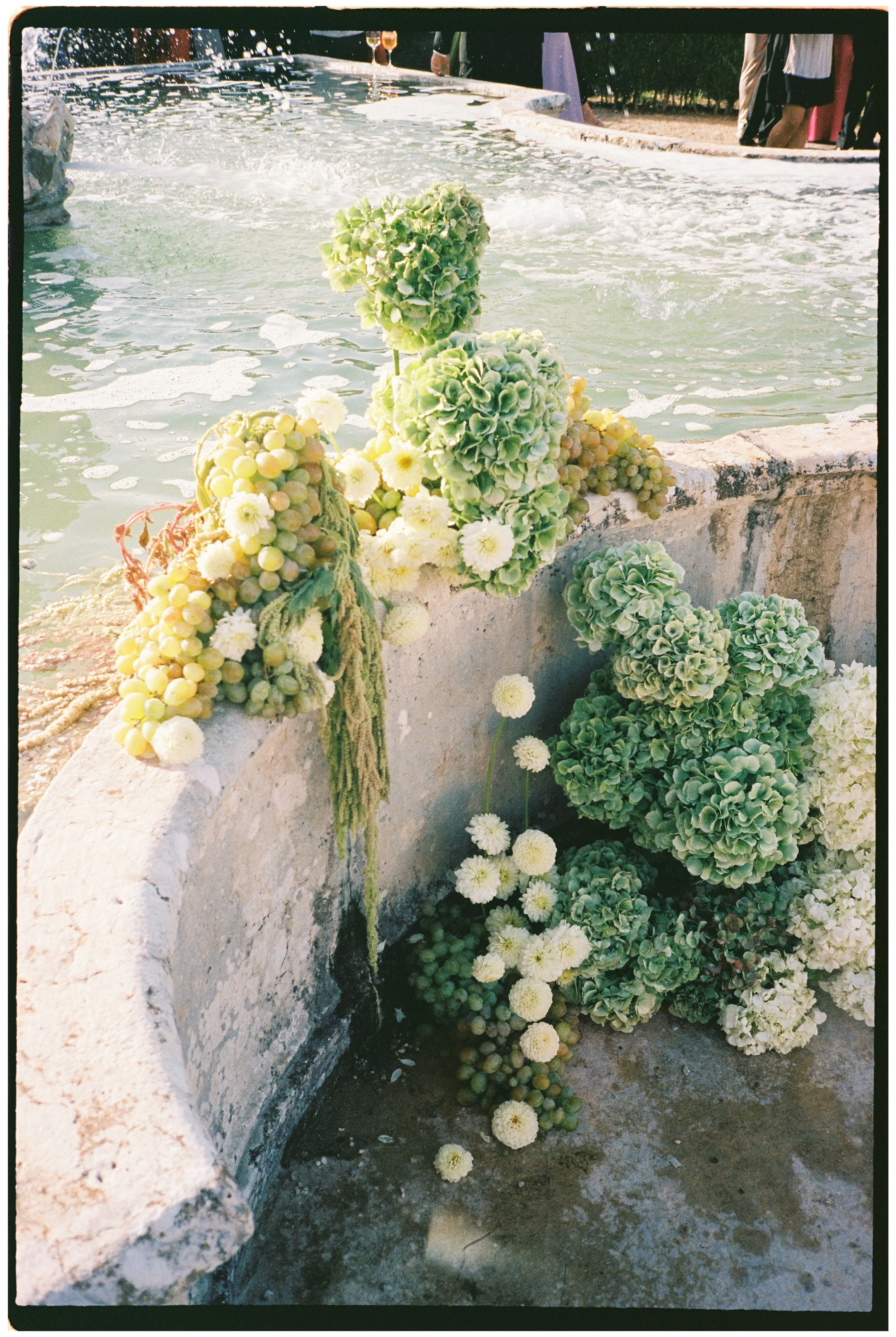 Wedding floral arrangement with hydrangeas and grapes decorating a fountain at Palácio do Correio-Mor in Portugal.