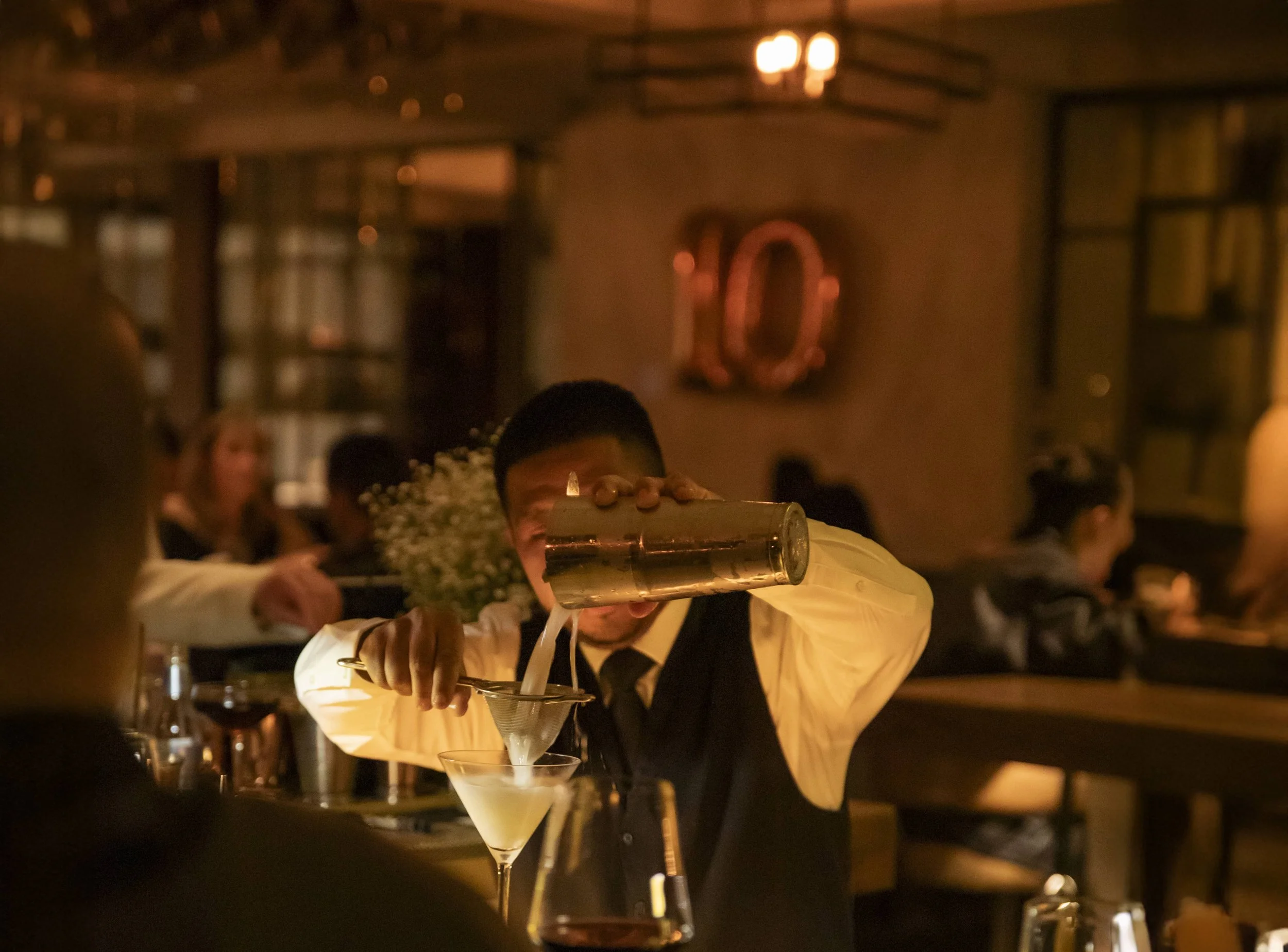 bartender pouring an opaque liquid from metal shaker into a martini glass