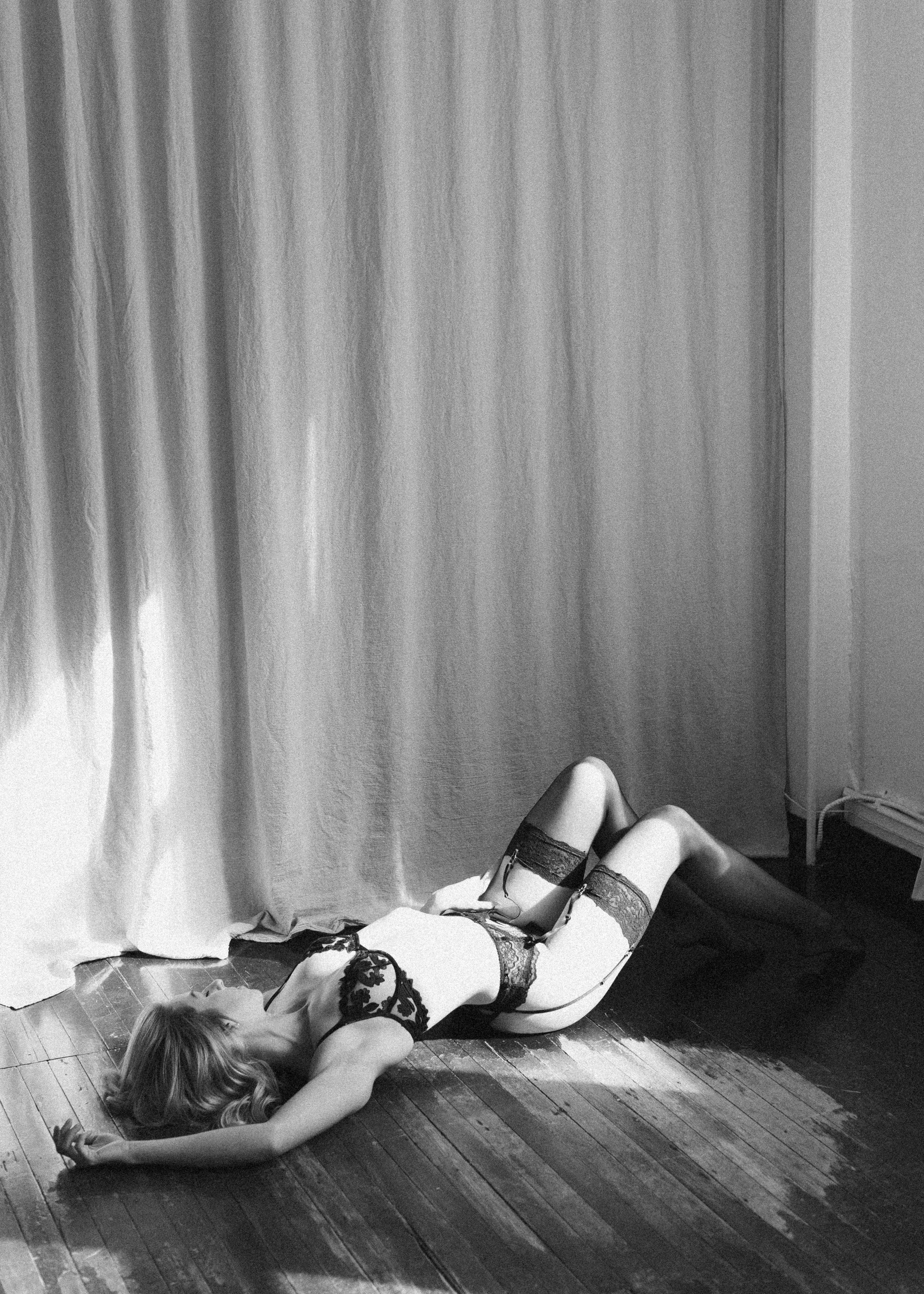 Woman lying on wooden floor in lingerie, black and white