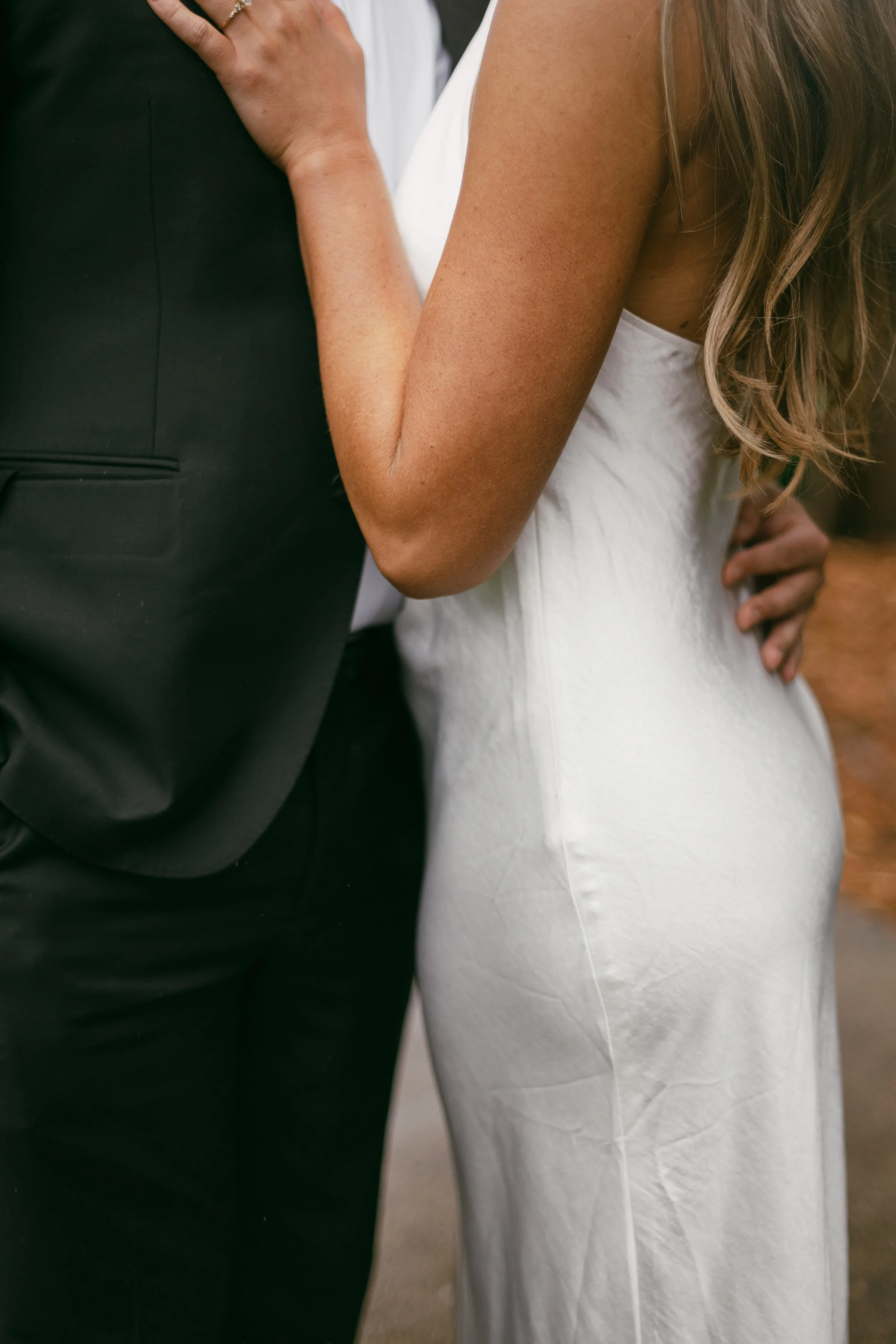 A bride and groom close together, the bride in a white dress with her arm around the groom in a black suit.