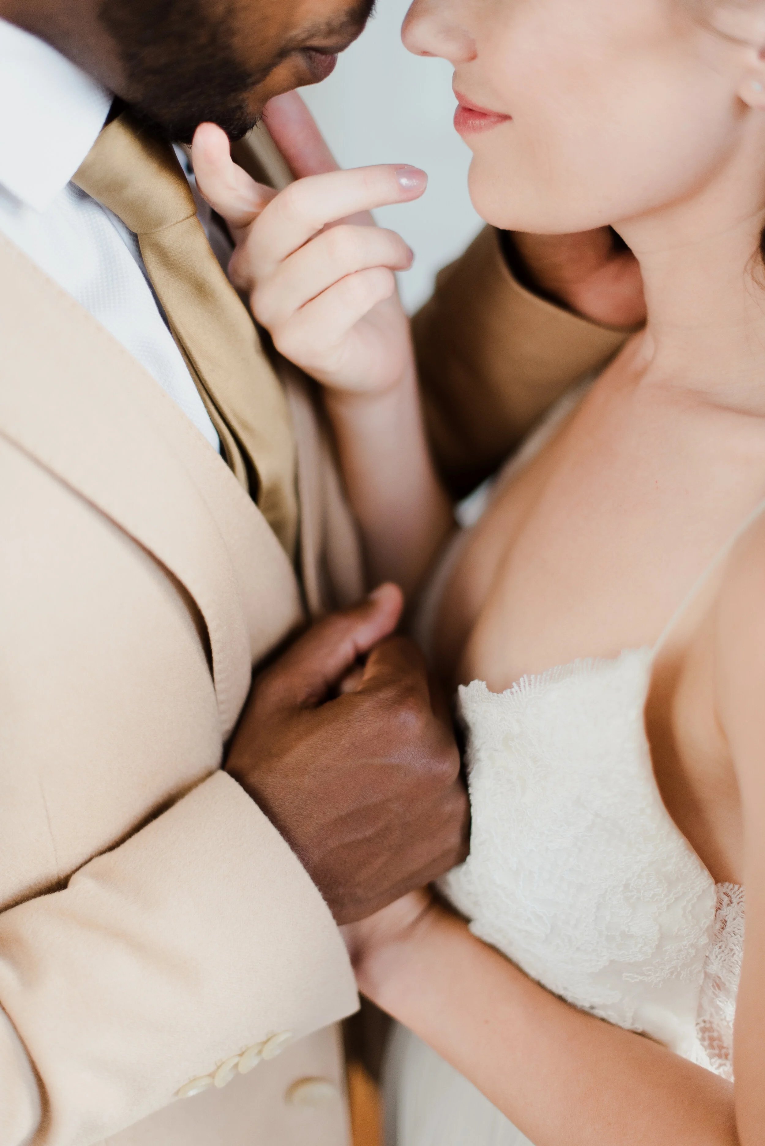 A close-up of a couple in an intimate moment, with the woman's face near the man's face, touching her lips with her finger, and the man's hand gently holding her arm.