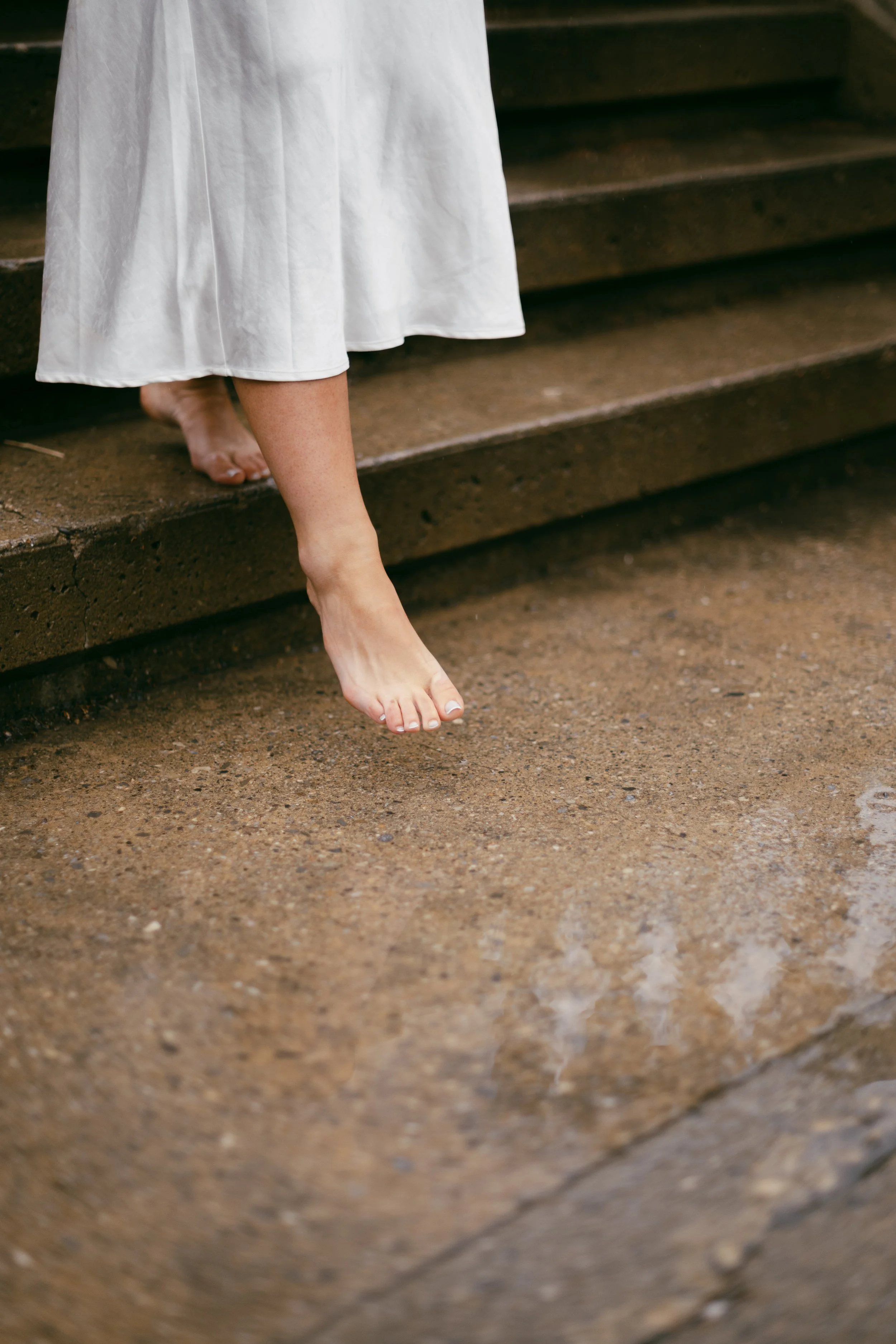Person with bare feet in a white dress walking down outdoor stone steps.