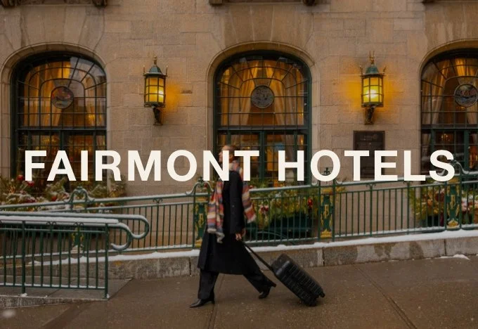 A person walking with a suitcase in front of a building with large arched windows and yellow lanterns, with the text 'Fairmont Hotels' overlaid.