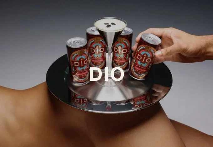 A person is holding a tray with cans of DIO energy drink and a glass of the drink with ice cubes. The background is gray.