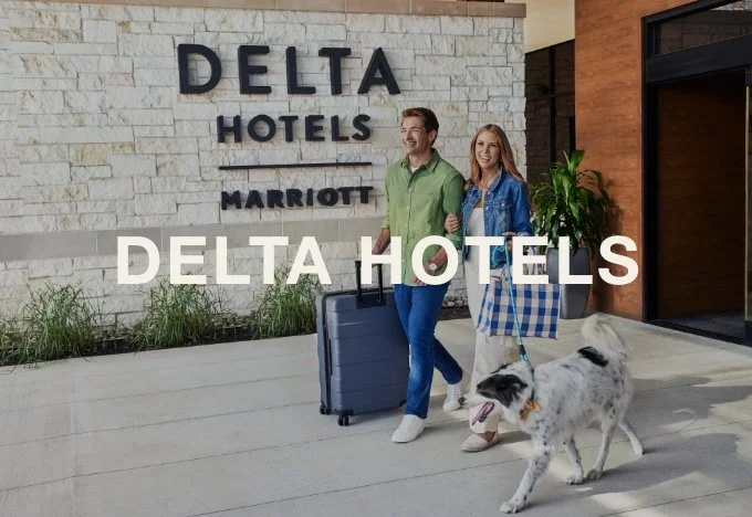 A couple walking their dog and carrying luggage outside the Delta Hotels Marriott building.