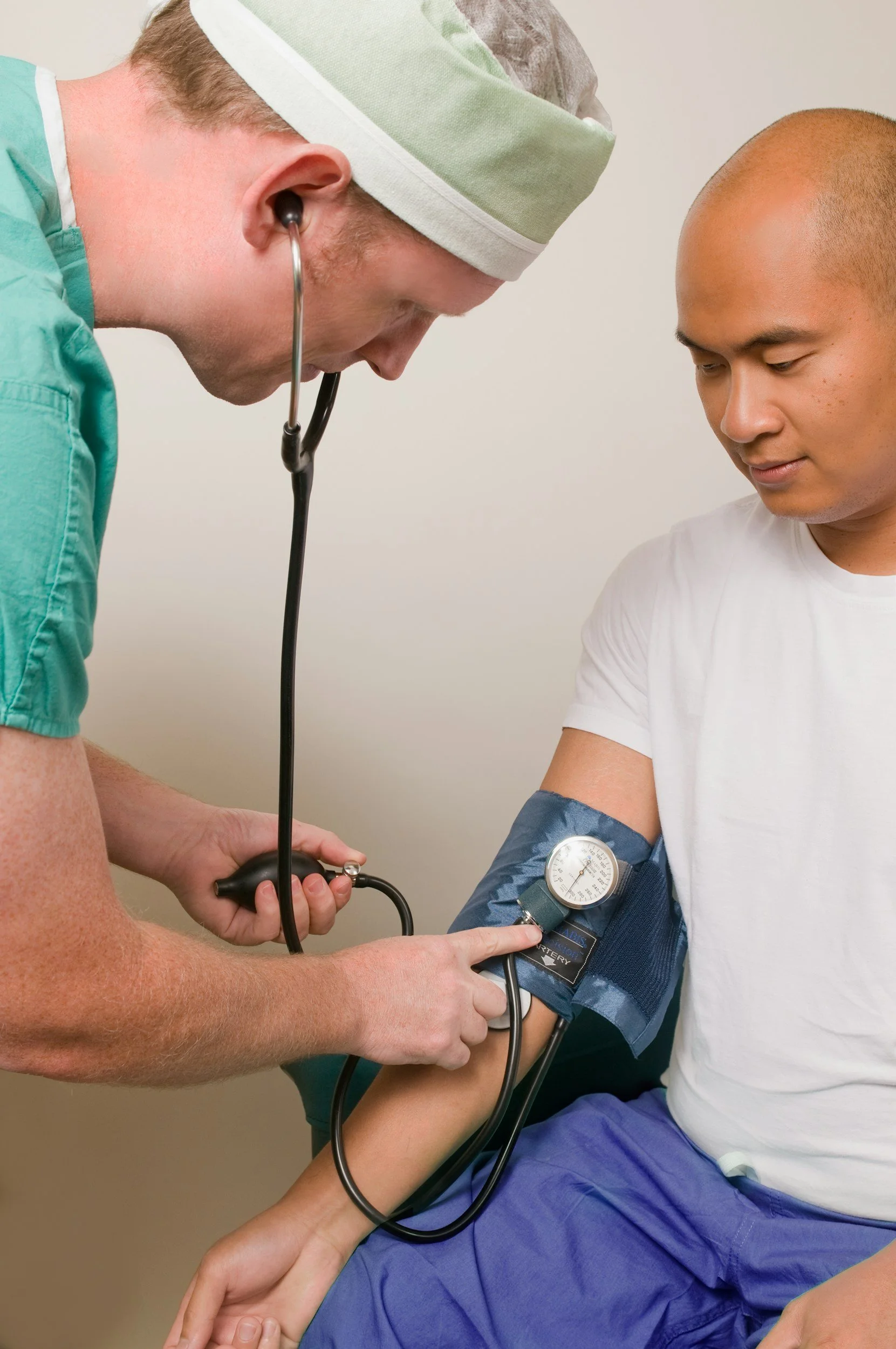A healthcare professional using a stethoscope to examine a young man with a blood pressure cuff on his arm.