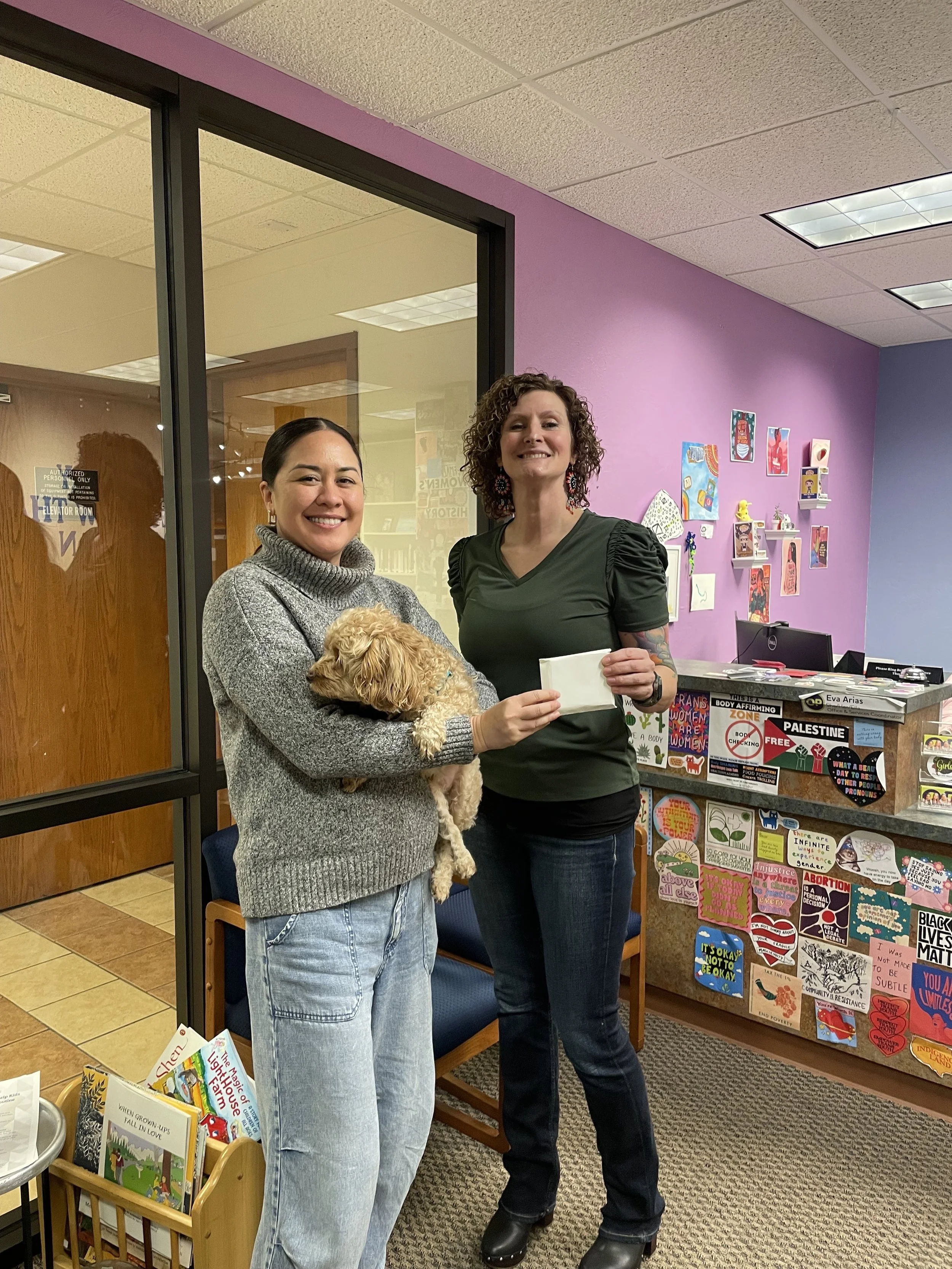 One woman hands a check to another woman holding a dog