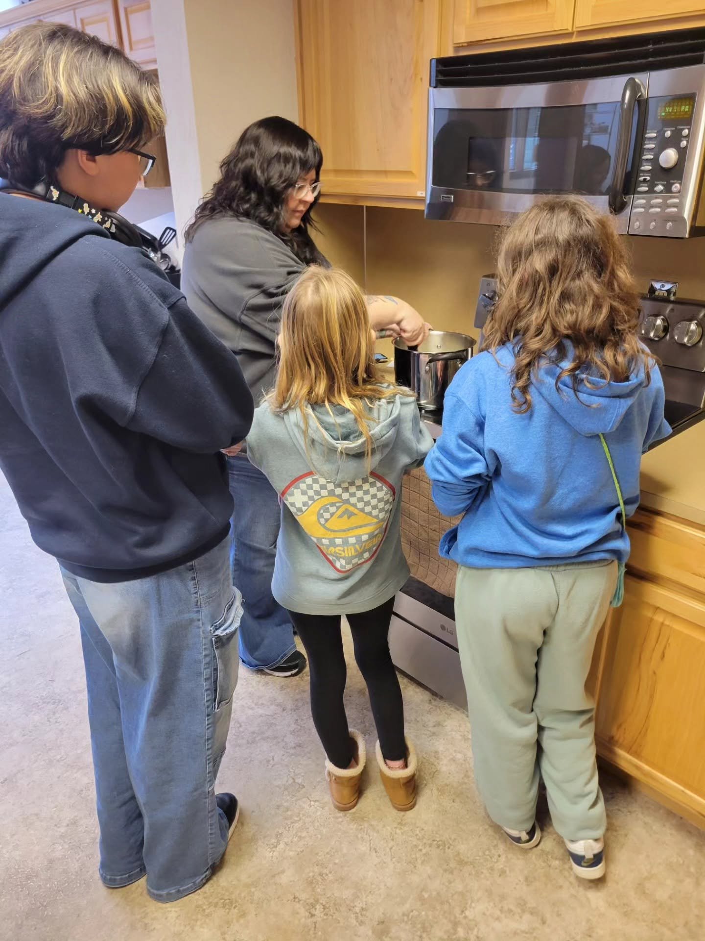 Three people watch and learn from an Ophelia's Place team member cook