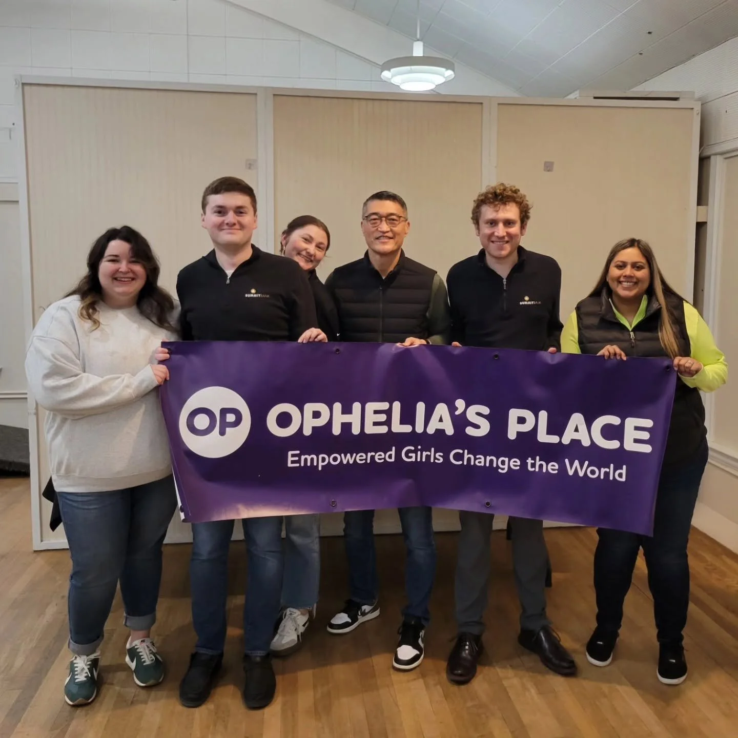 Six people hold up banner for Ophelia's place in an event space