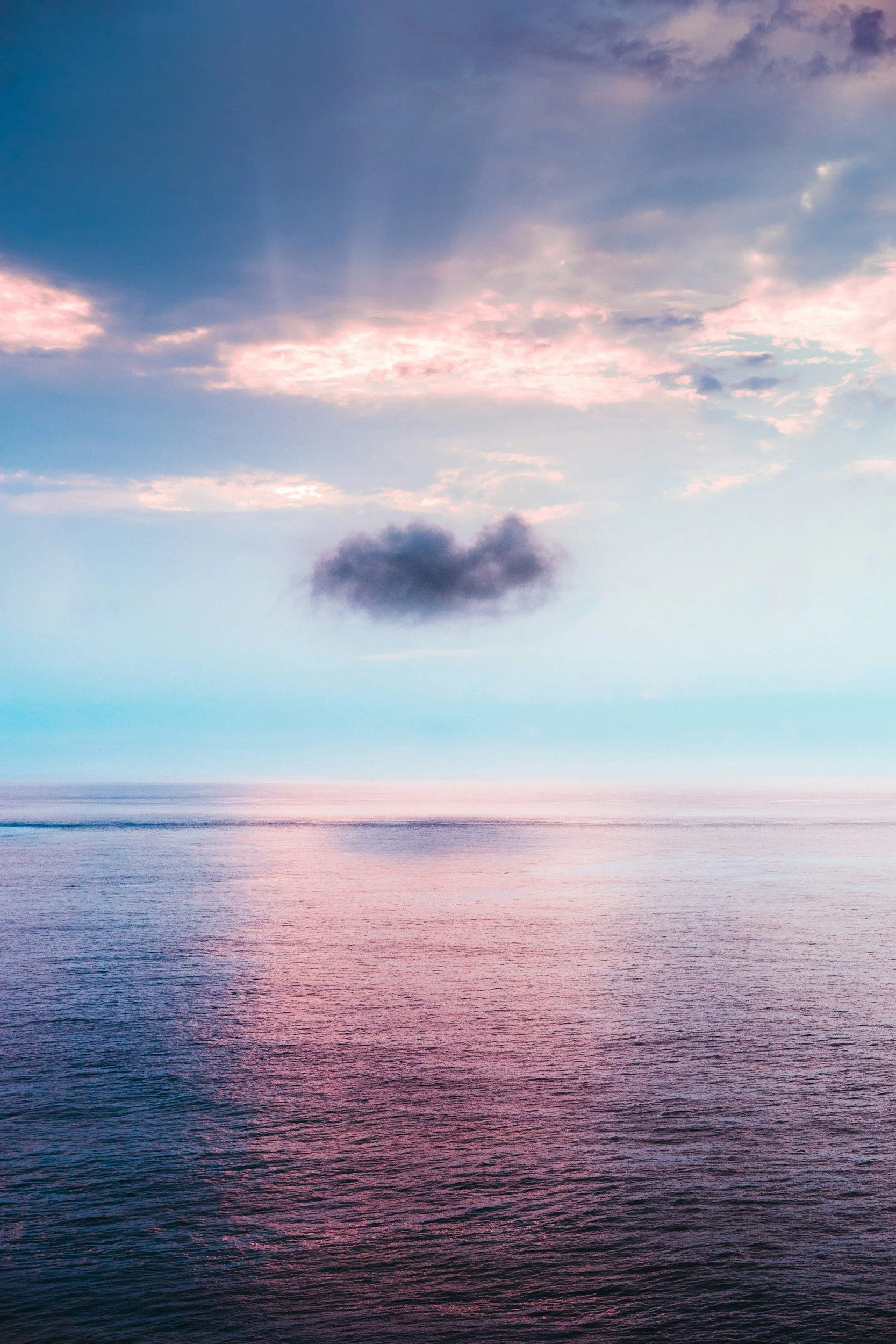 Calm ocean under a colorful twilight sky with pink and blue clouds and a dark cloud in the center.