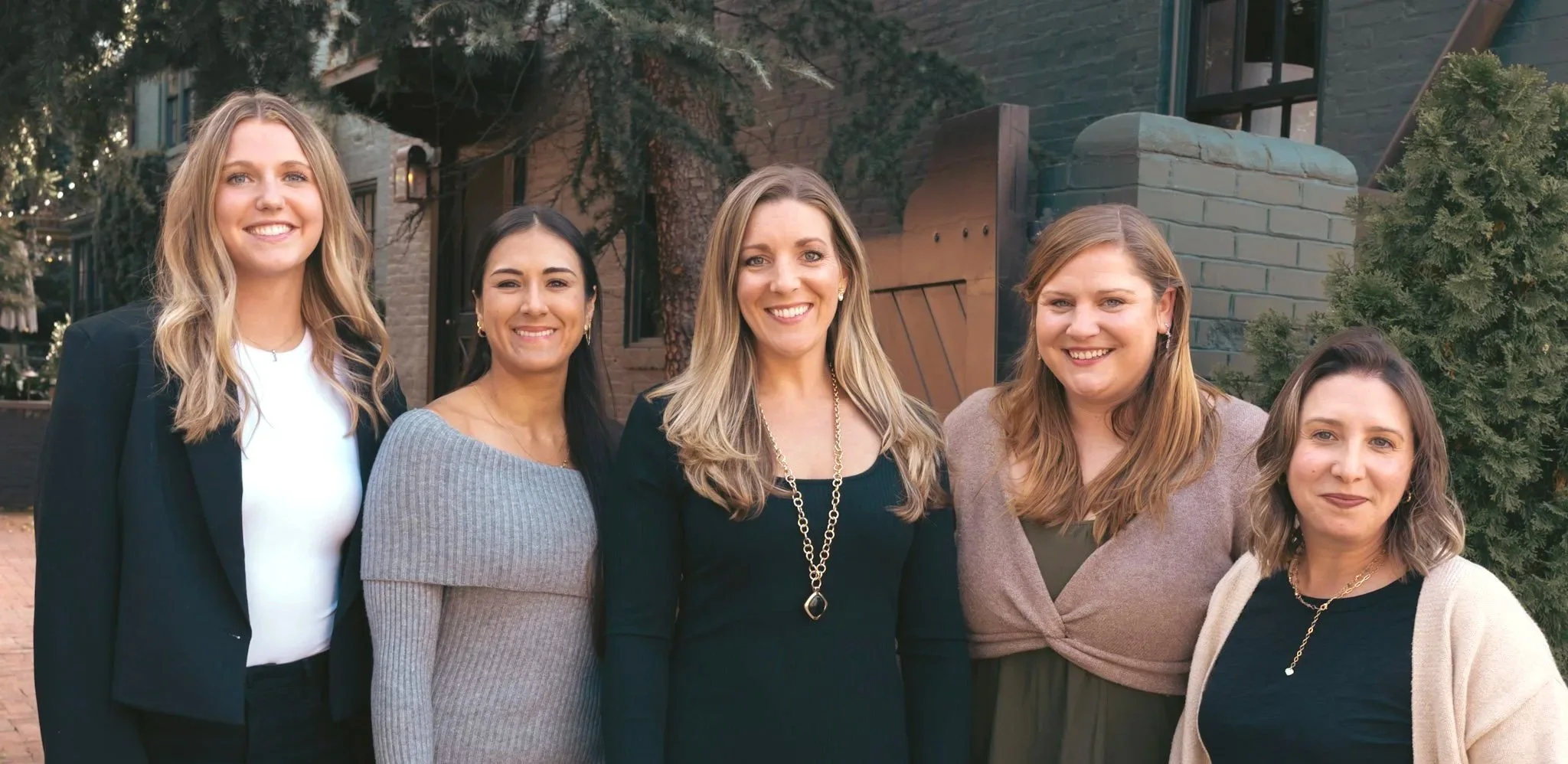 Six women standing outdoors in front of a building, smiling at the camera.